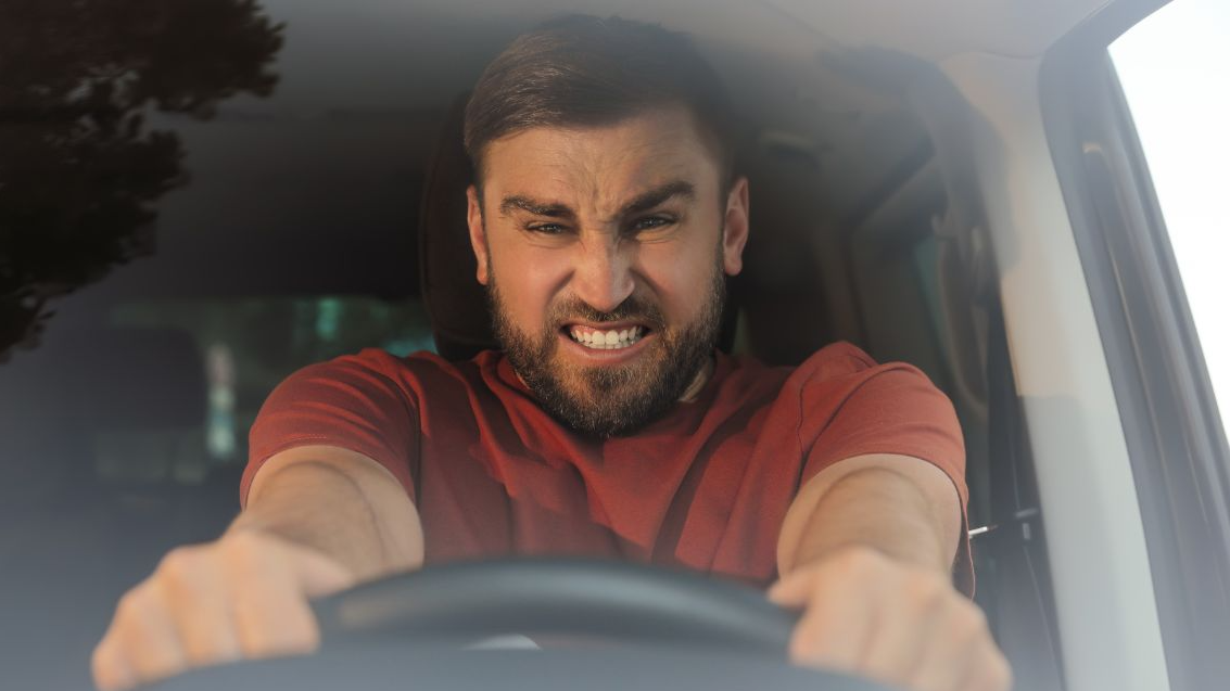 Emotional man in car, view through windshield. Aggressive driving behavior