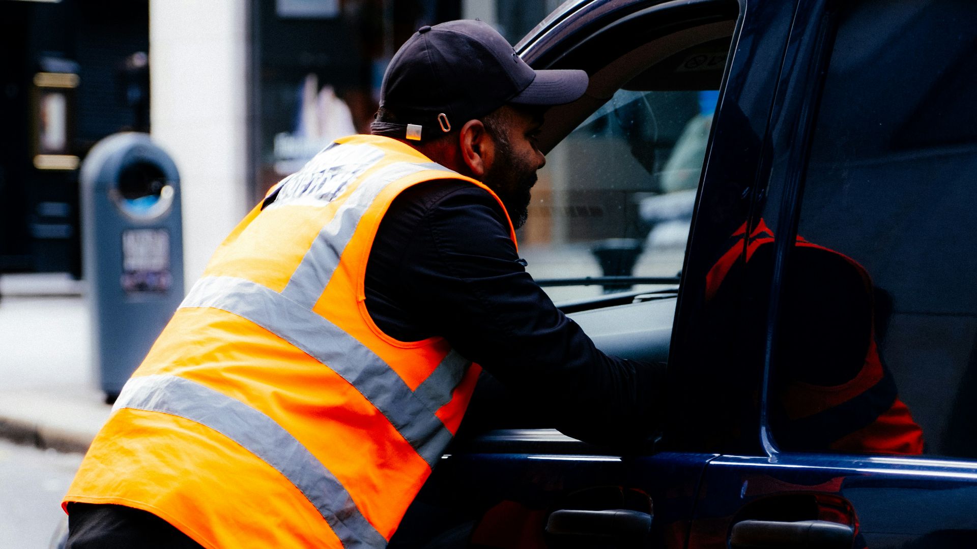 Man in high-visibility vest leans into car.