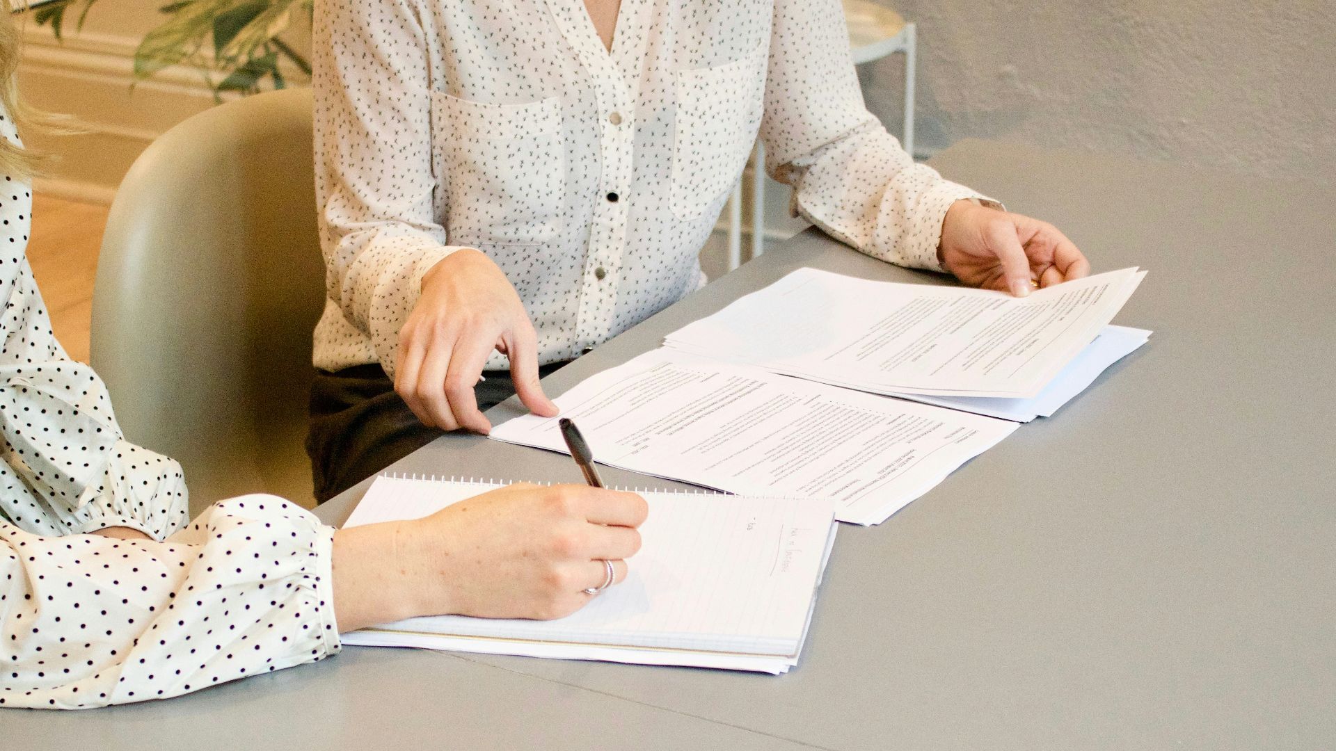 woman signing on white printer paper beside woman about to touch the documents