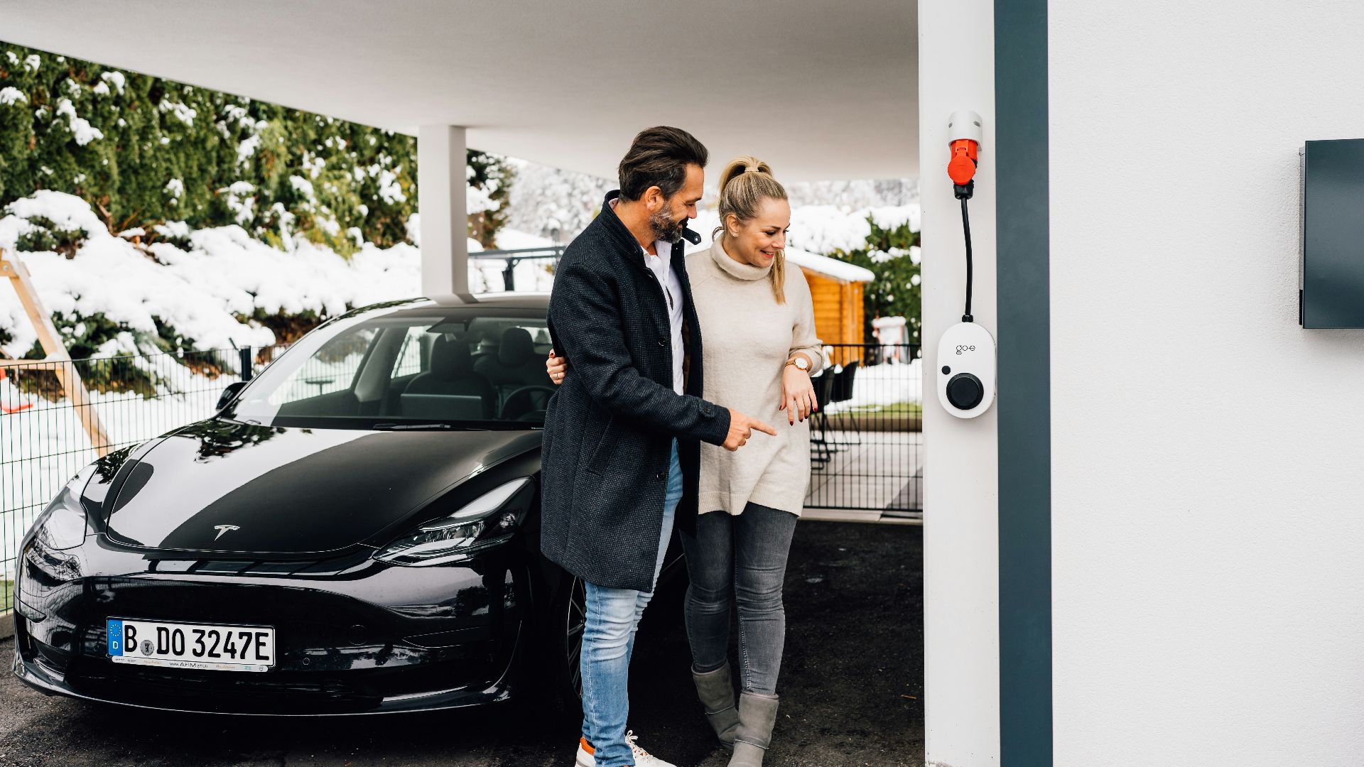 Couple by their electric car next to a charger.