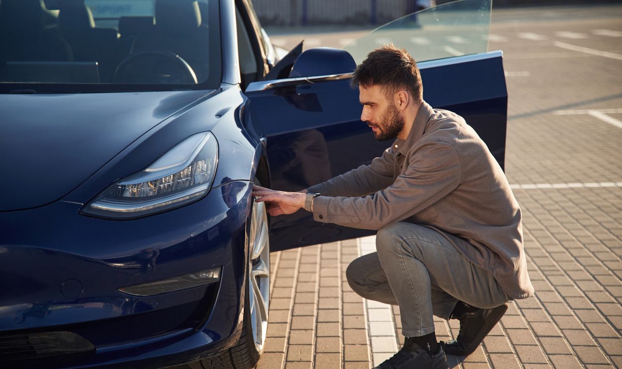 Sitting and checking the wheel. Man is standing near his electric car outdoors.