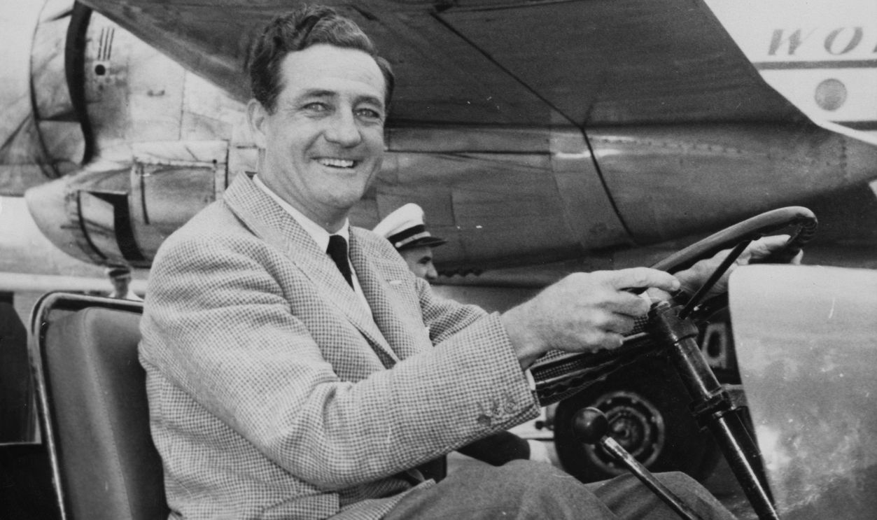 American entrepreneur Briggs Cunningham (1907 - 2003) drives a luggage cart at Orly Airport near Paris, France, having arrived to take part in the 24 Hours of Le Mans sports car race, 2nd June 1954.