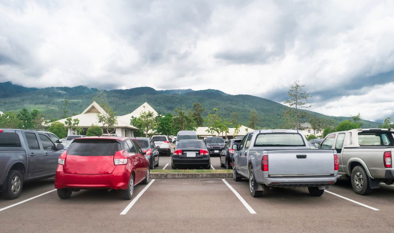 Car parked in asphalt parking lot and one empty space parking in nature with trees, beautiful cloudy sky and mountain background .Outdoor parking lot with fresh ozone and green environment concept