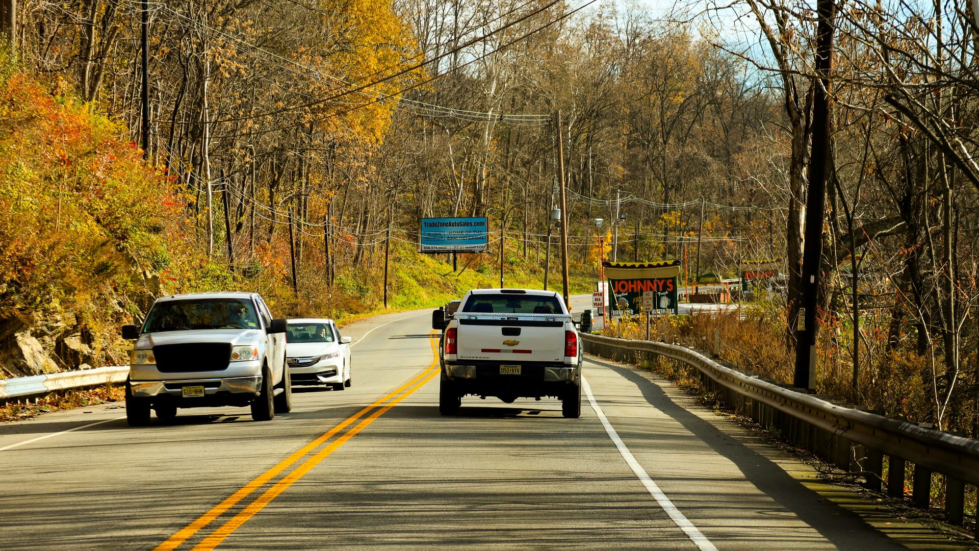 Cars driving on a road beside autumn trees
