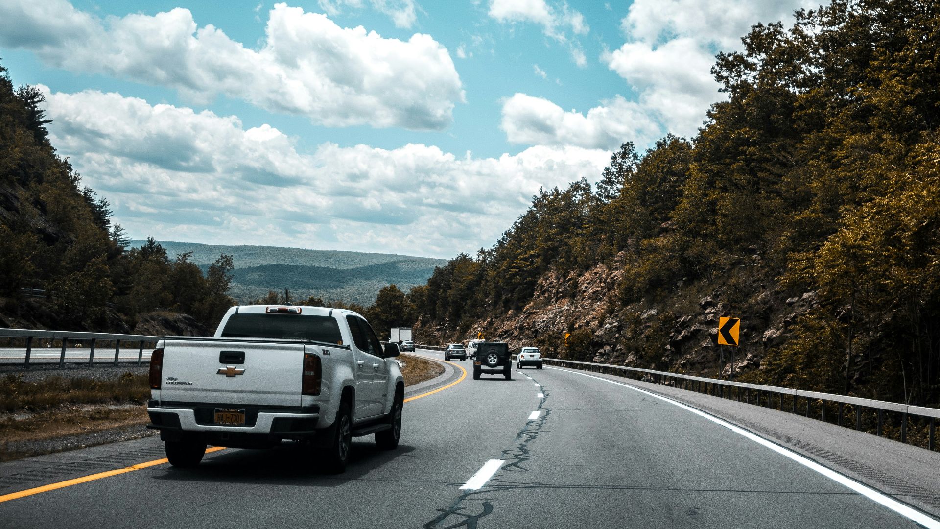 a white truck driving down a road next to a forest