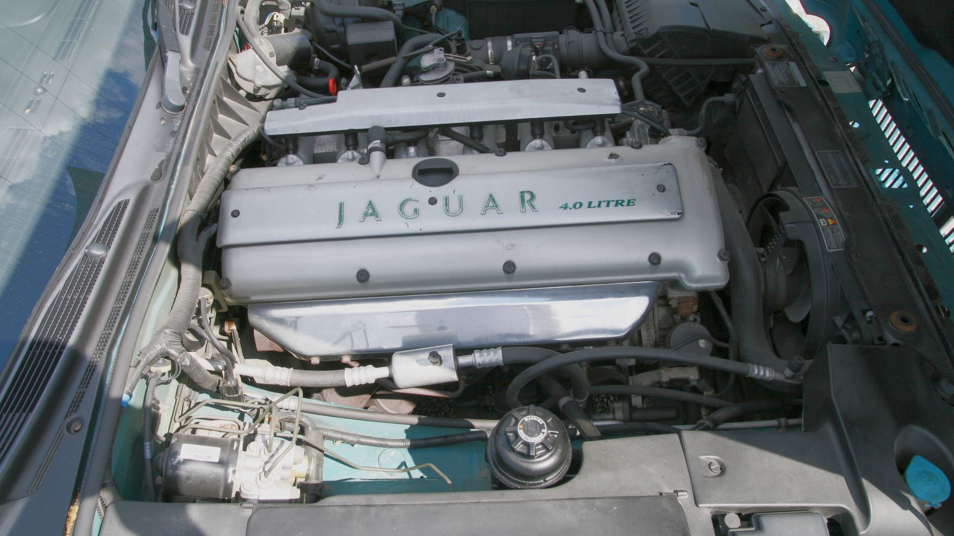 Right-hand side view of the engine bay of a 1995 Jaguar XJ, showing the naturally aspirated 4.0 liter AJ16 engine. The chromed exhaust manifold cover reveals this as a 1995 model year car.