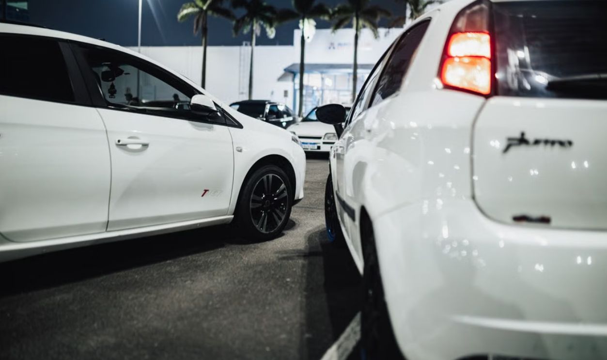 White cars gathered at a nighttime car meet in an illuminated parking lot