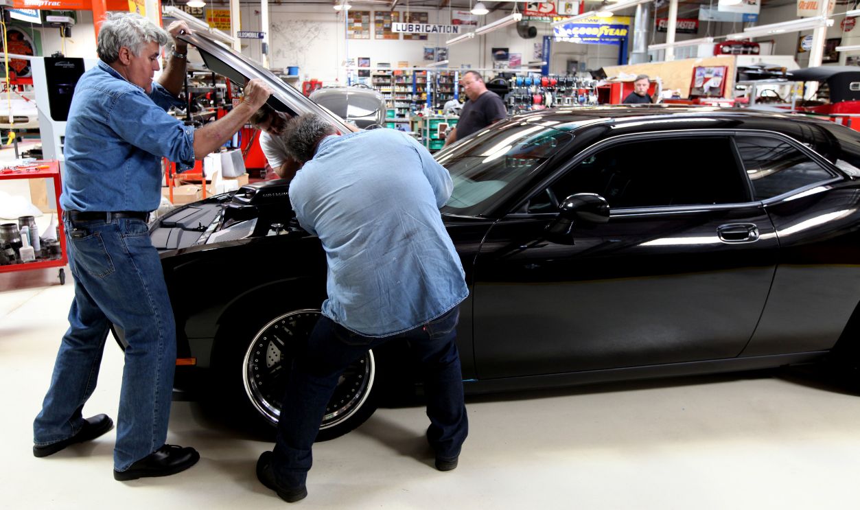 Getty Images - 526204688 - Nightly talk show host and comedian Jay Leno helps crewmen assemble parts on a Dodge Challenger at his car garage in Burbank, California.