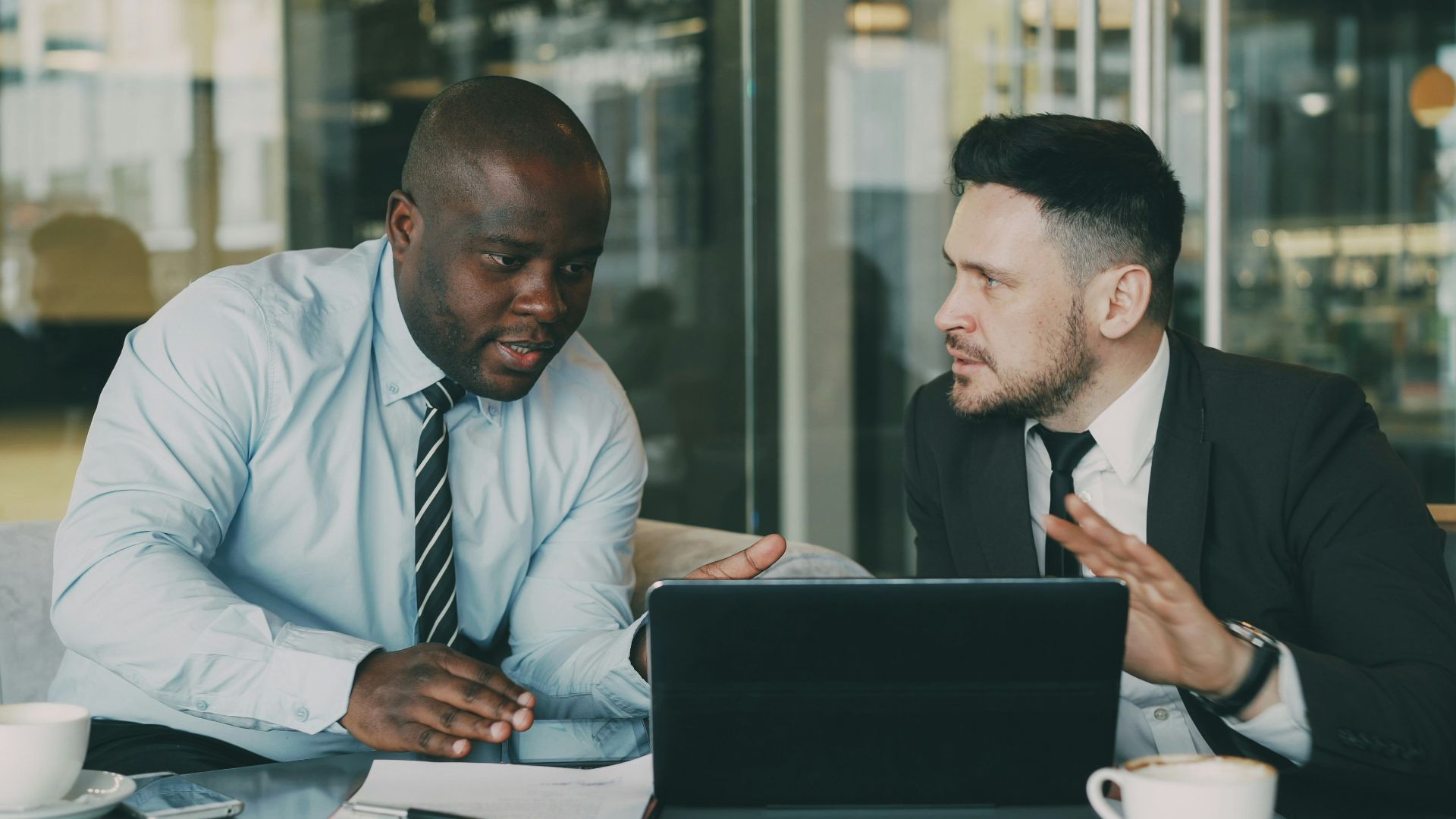 Two businessmen collaborating over a tablet and laptop