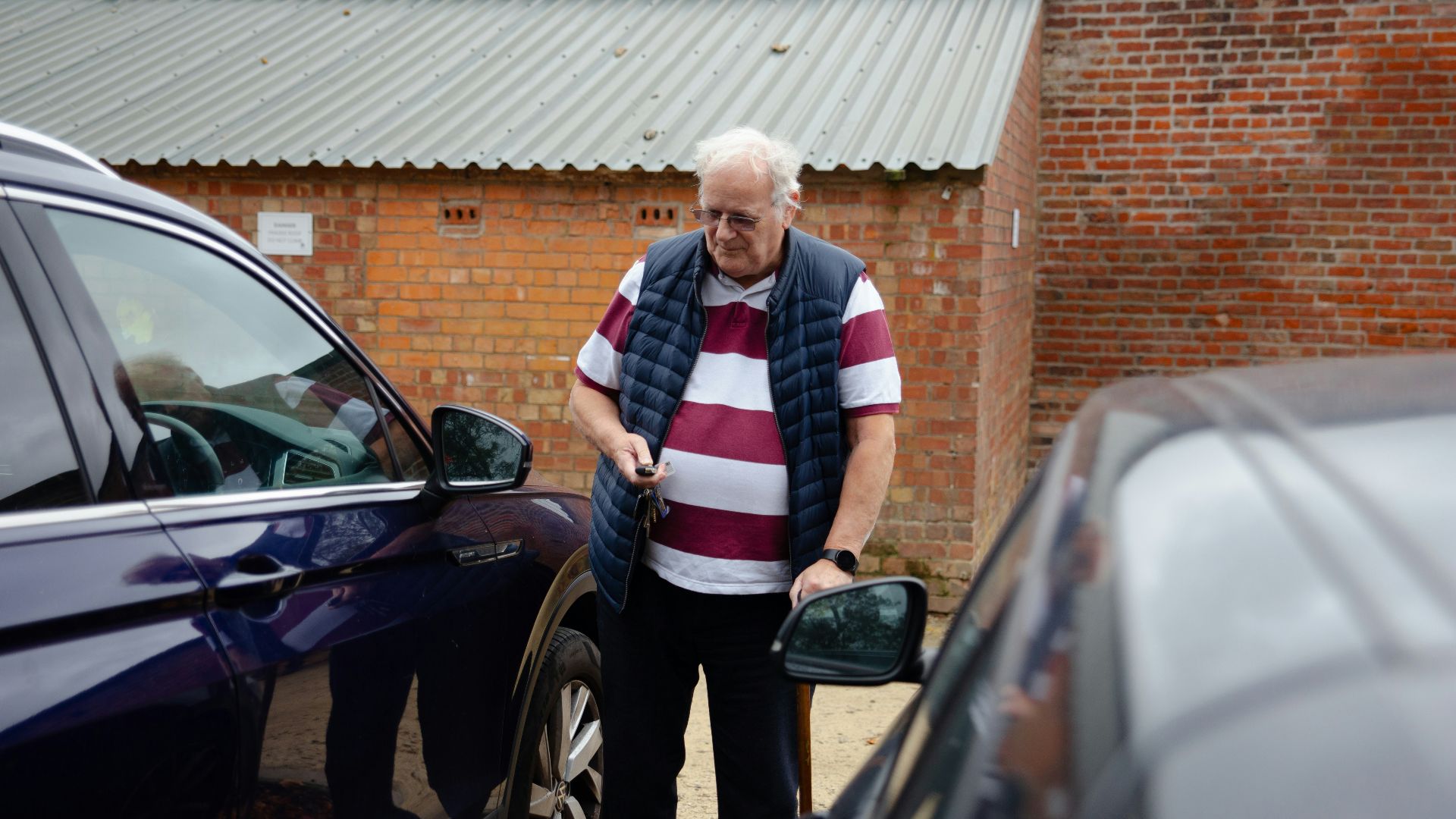 An older man stands between two cars