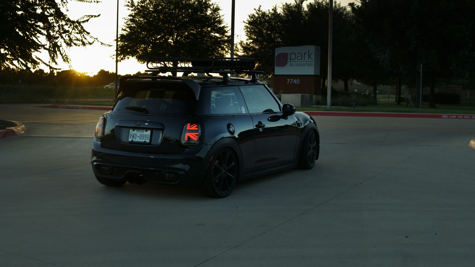 Black mini cooper with roof rack driving at sunset