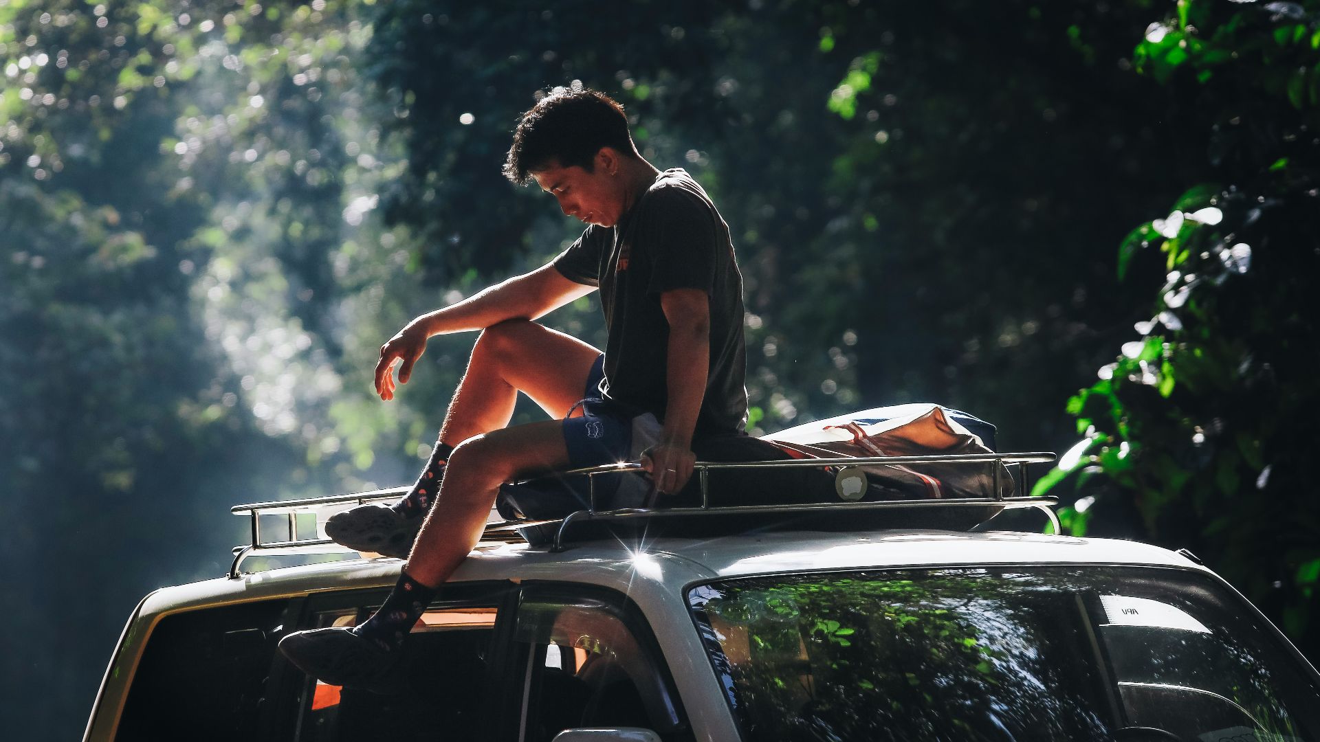 Young man sitting on top of a car roof