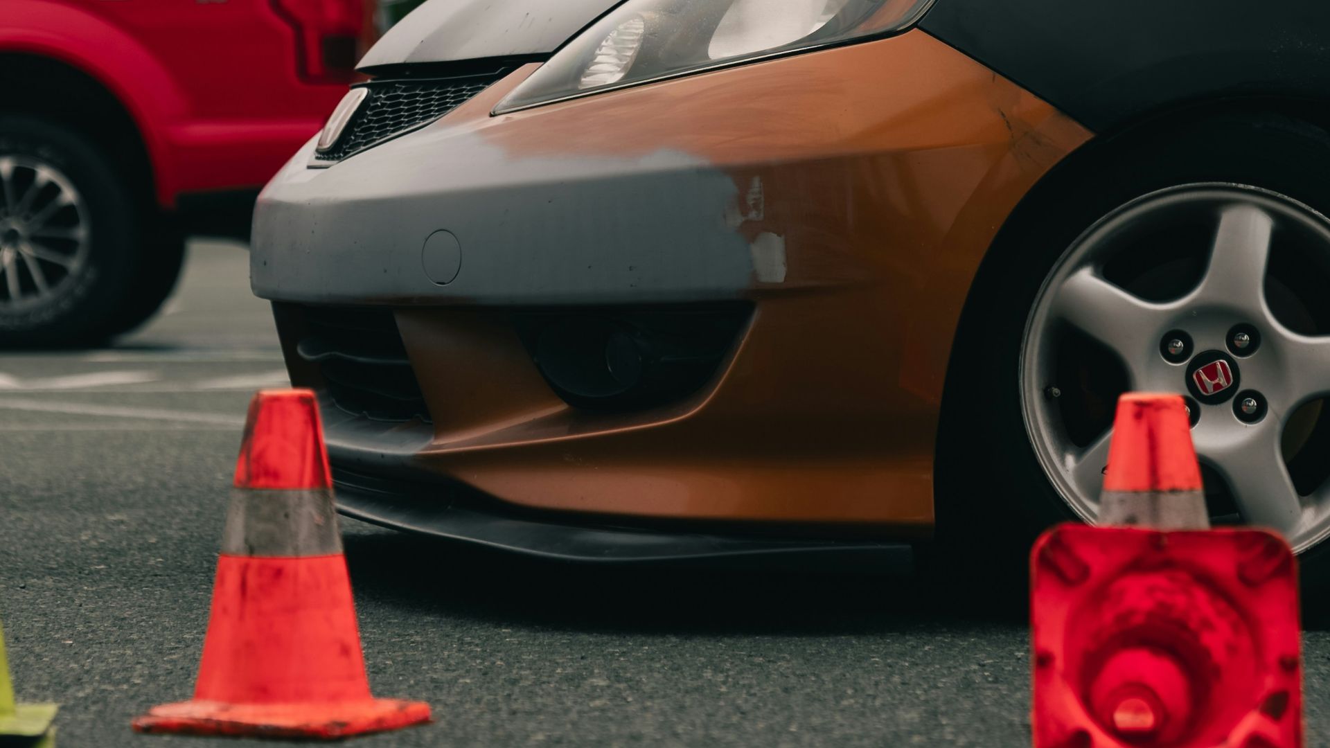 A car with a mismatched grey bumper and orange body in a parking lot