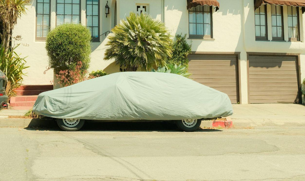 Vintage Mediterranean house with car covered in the driveway under a bright sky.