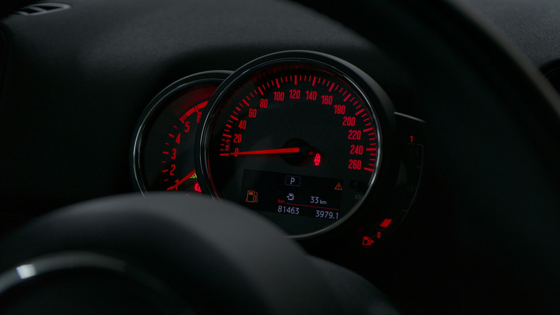 A car speedometer with glowing red numbers and needles in a dark interior