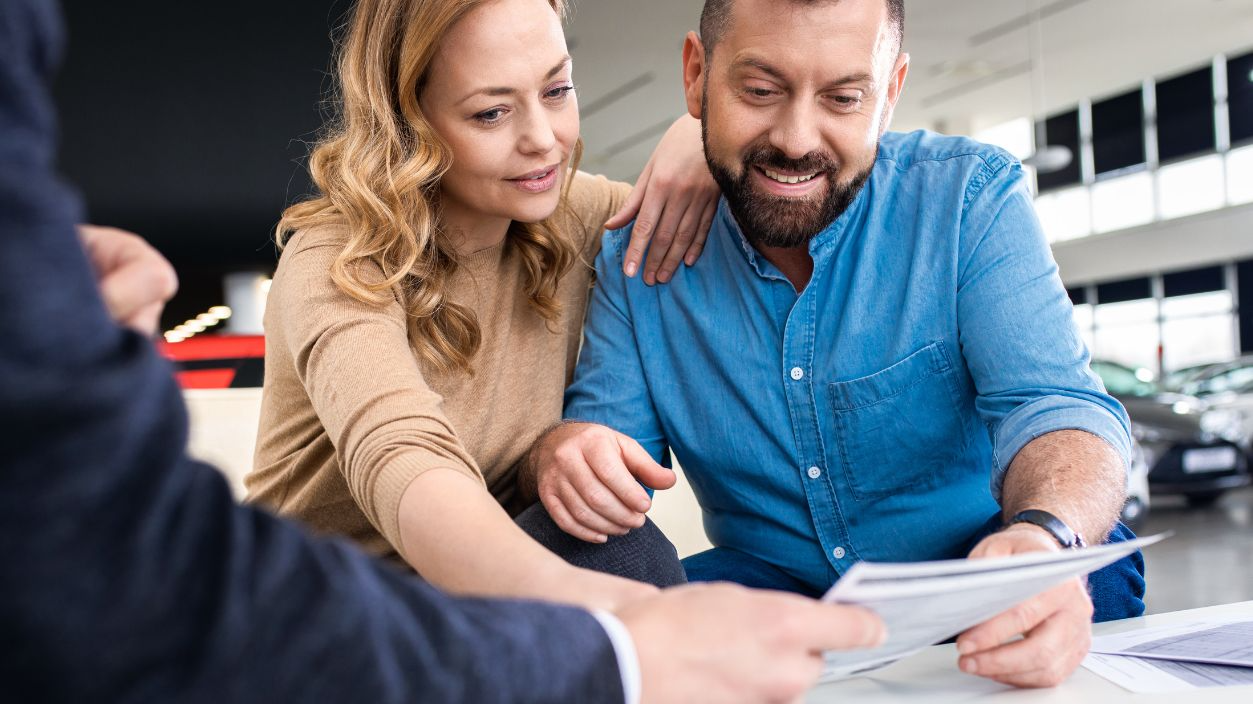 Shutterstock-1875108832, Mid-adult couple talking with sales agent and signing contract for new car in modern car showroom.