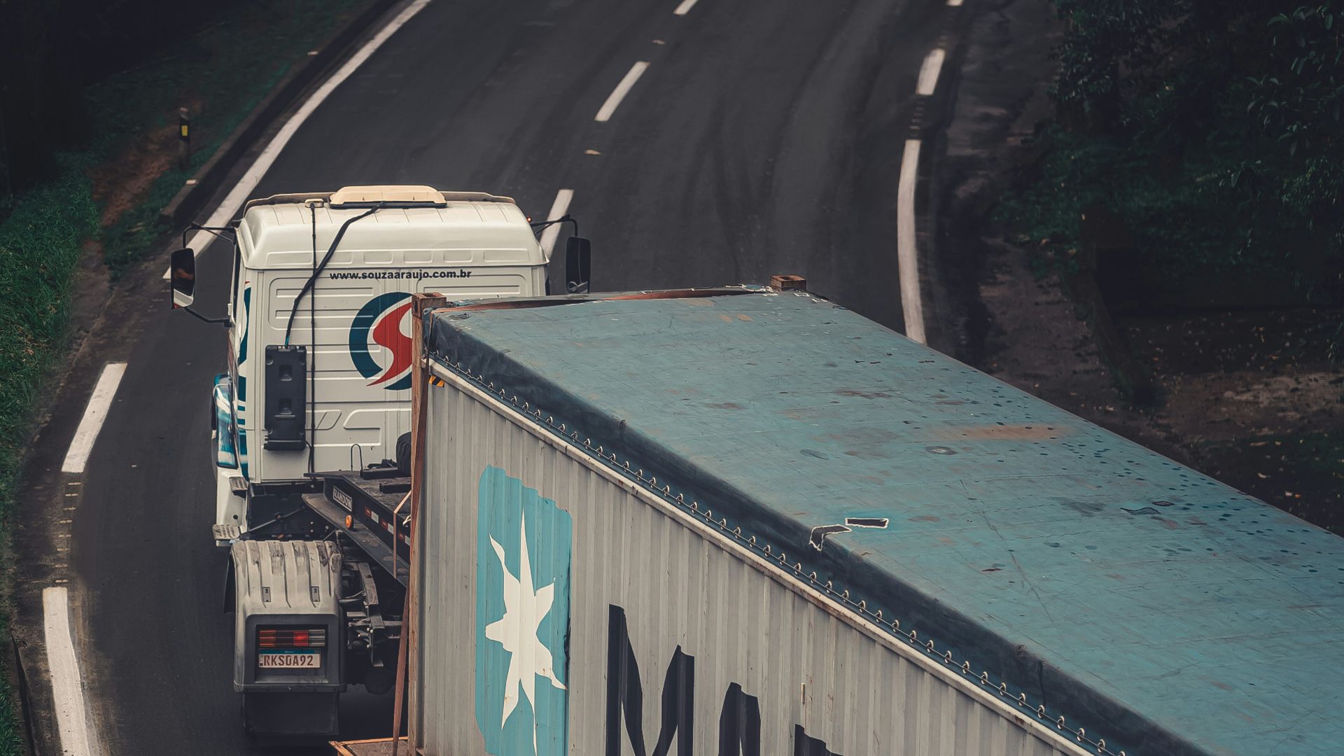a semi truck driving down a road next to a forest