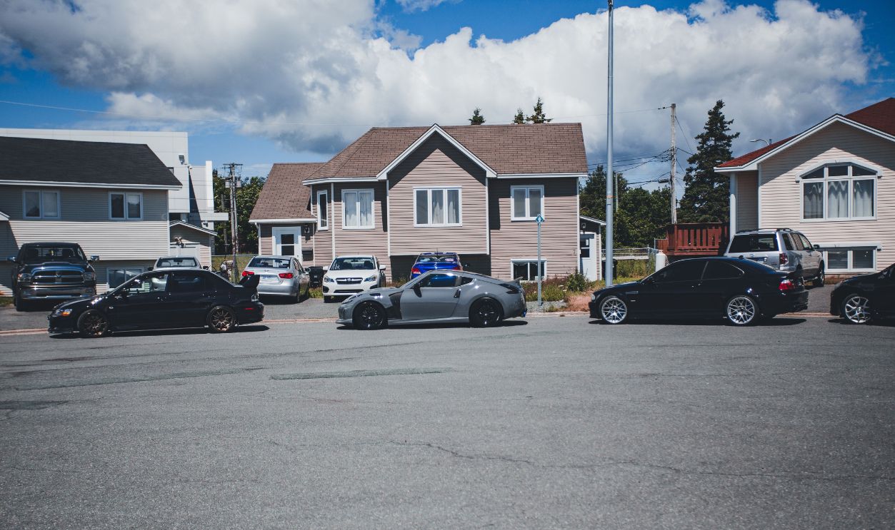 Sunny neighborhood street with modern homes and parked vehicles on a bright day.