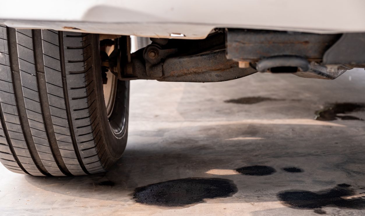 Shutterstock - 2776067689 - Close-up of oil leaking from a car onto a concrete floor. Concept of vehicle breakdown, mechanical failure, engine oil leak, maintenance issues, and the need for automotive repair services.