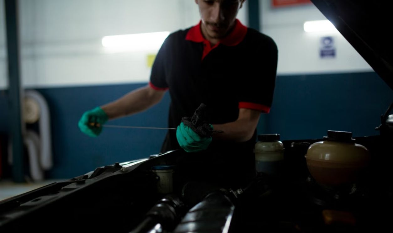 Mechanic examining a car engine's oil level using a dipstick in a garage setting.