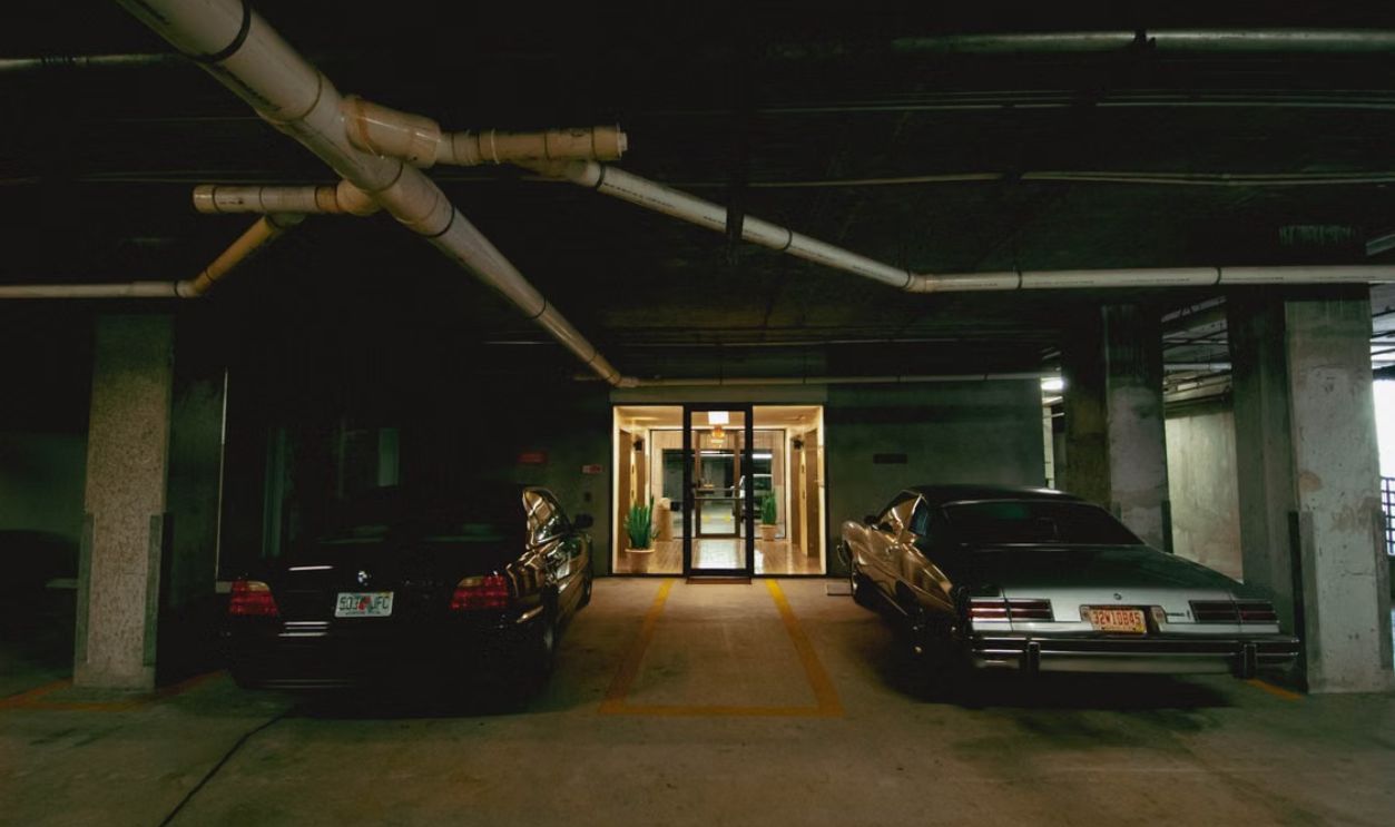 Two cars parked in a dimly lit underground parking garage with visible pipes.