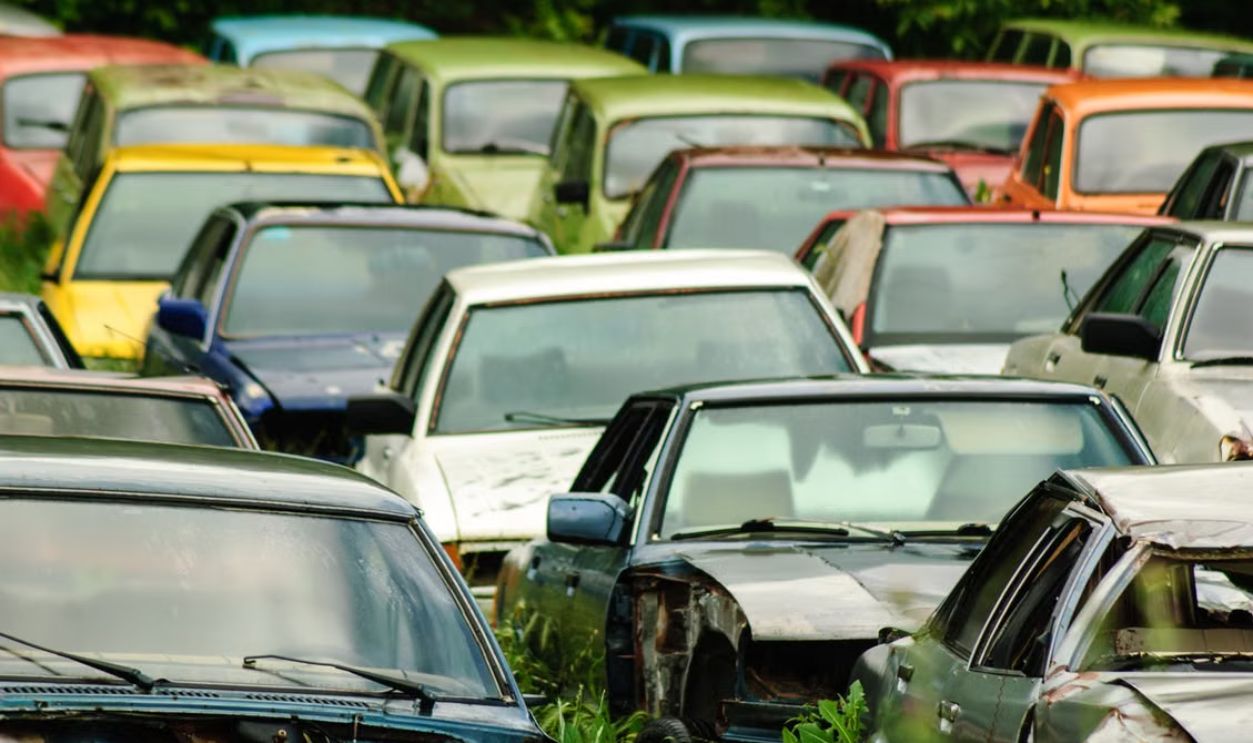 A collection of colorful vintage cars abandoned in a rural field, showcasing decay and history.