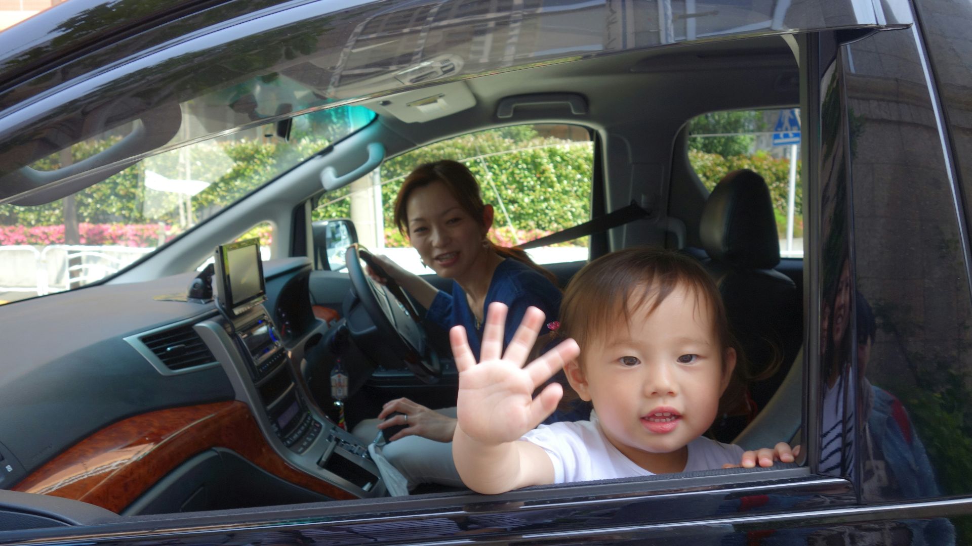 Child waves from car window with mother driving
