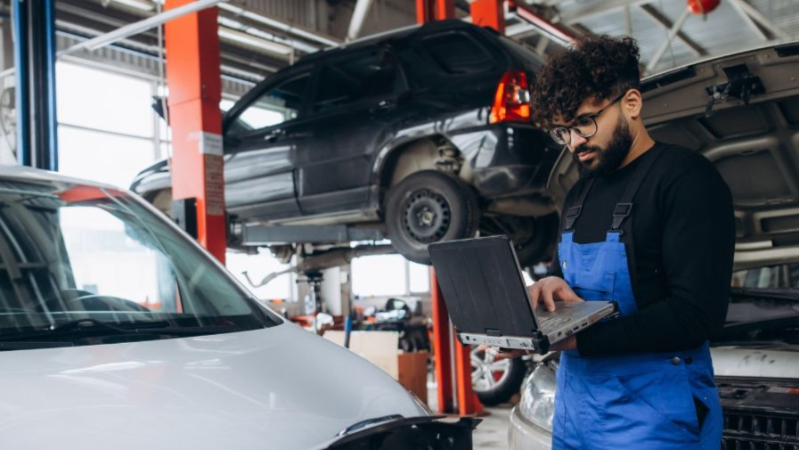 Shutterstock-2736596487, Professional mechanic performing diagnostic check on an electric vehicle with a laptop in a modern auto repair workshop