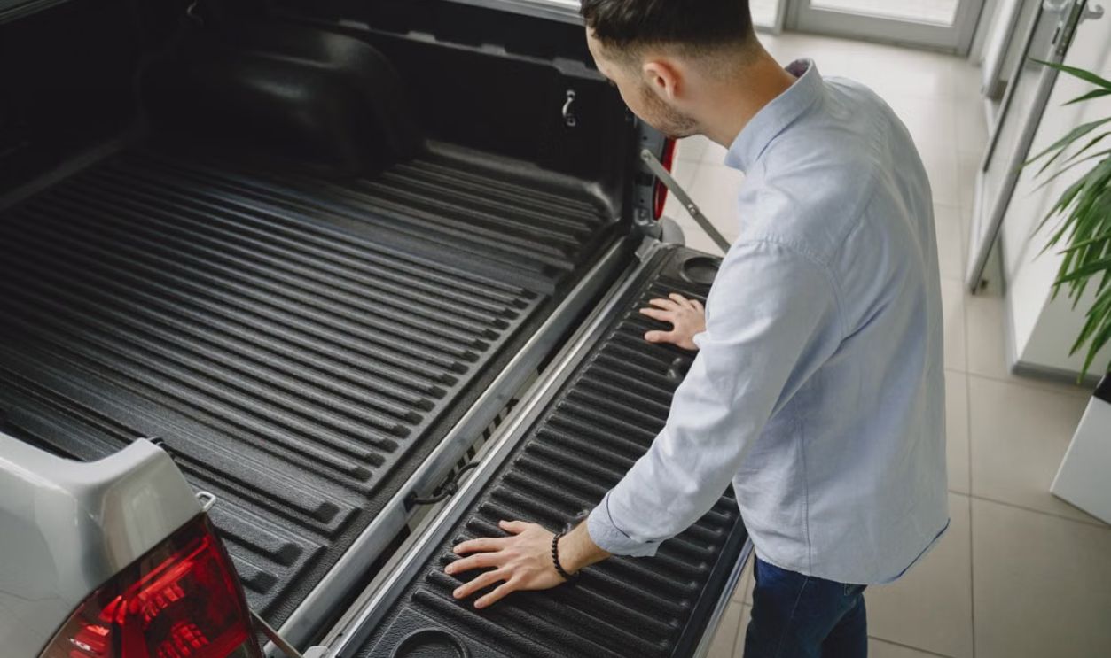 Adult man examines tailgate of a new pickup truck in a vehicle showroom.