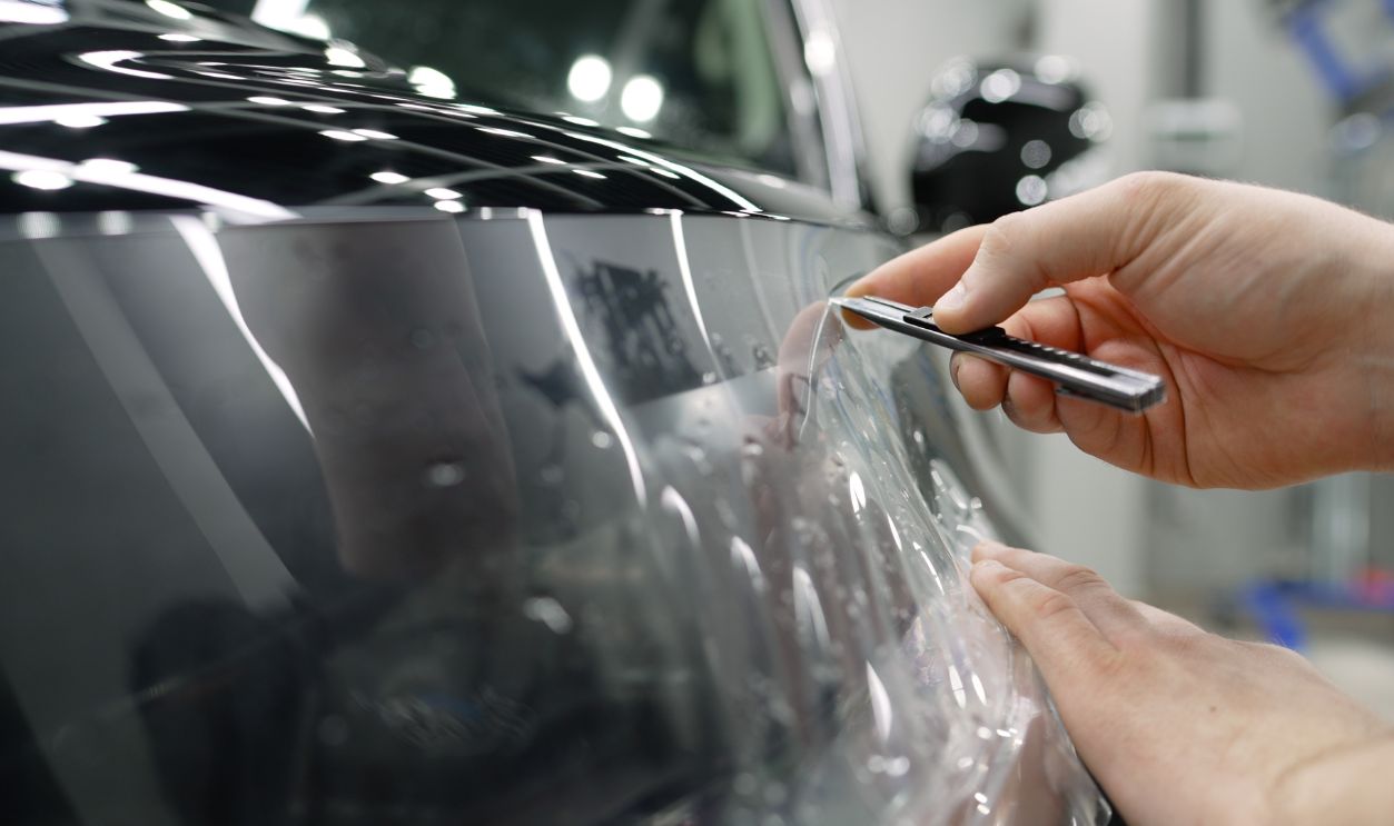 Skilled professional precisely applying protective vinyl film on luxury vehicle surface within workshop garage setting