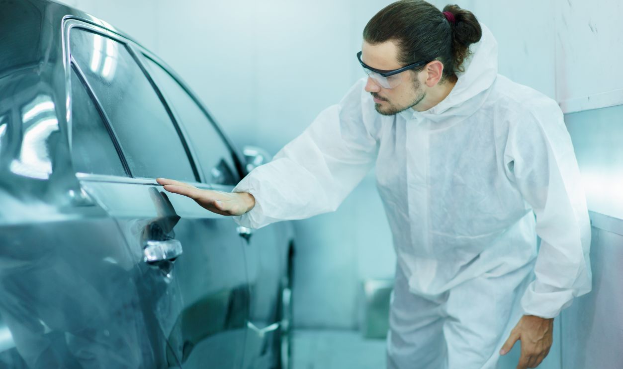 Shutterstock-2294743817, Professional automotive painting technician in chemical protecting suit inspecting car painting quality in painting chamber together. Car painting and detailing technicians portrait.
