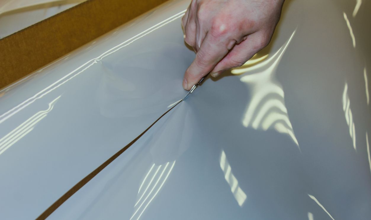 A man cuts off a polyurethane film with a knife.  The process of cutting off the desired piece of PPF. PF anti-gravel, protective film for paint coatings.