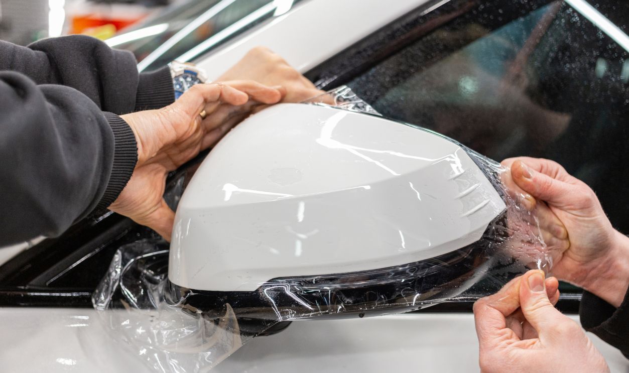 The process of installing PPF on the side of the car. PPF is a polyurethane, protective film that protects the paint from scratches and gravel. Armored film on the car mirror. Car wrapping close-up.