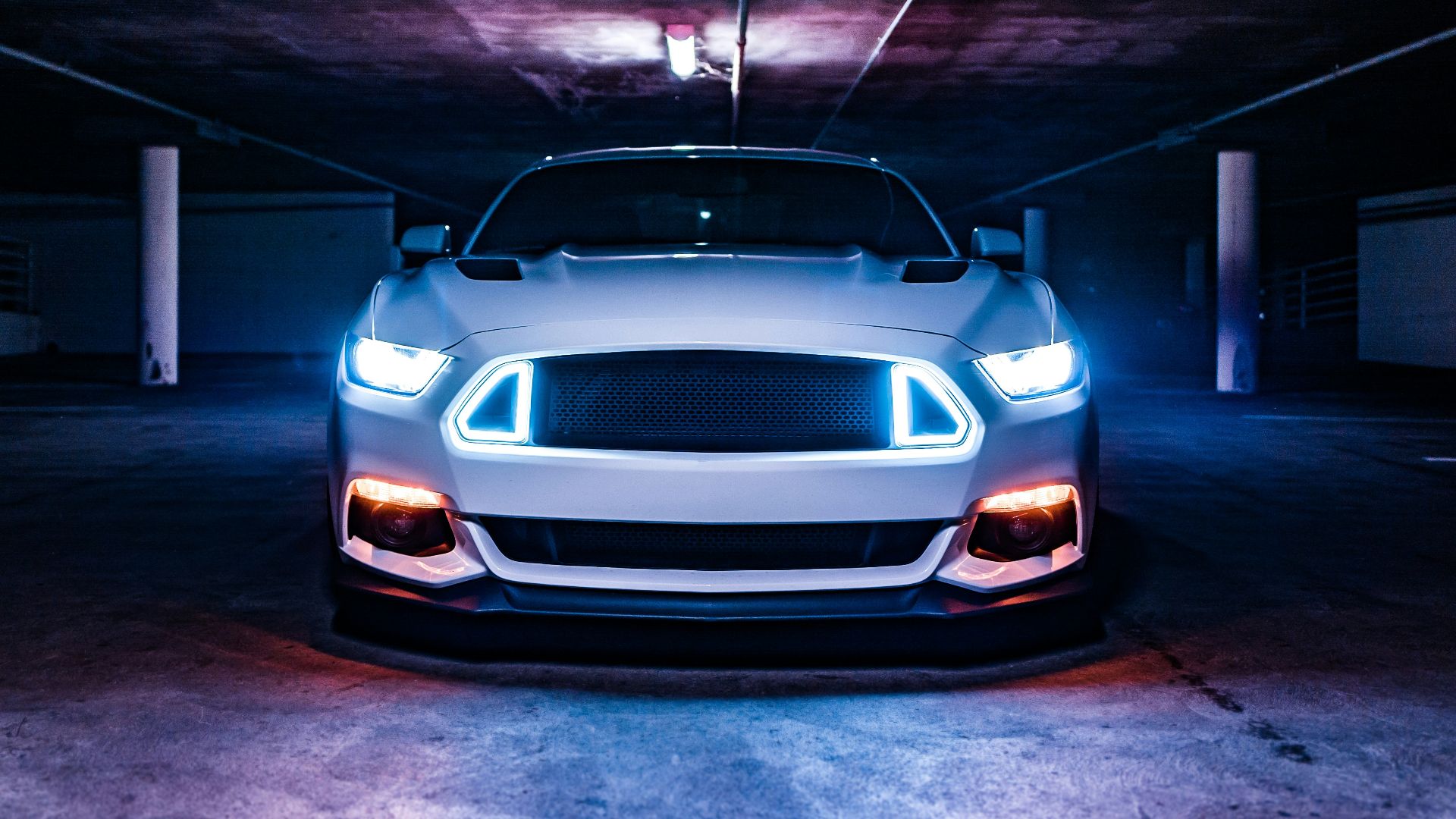A white sports car with glowing blue headlights in a dark concrete parking garage
