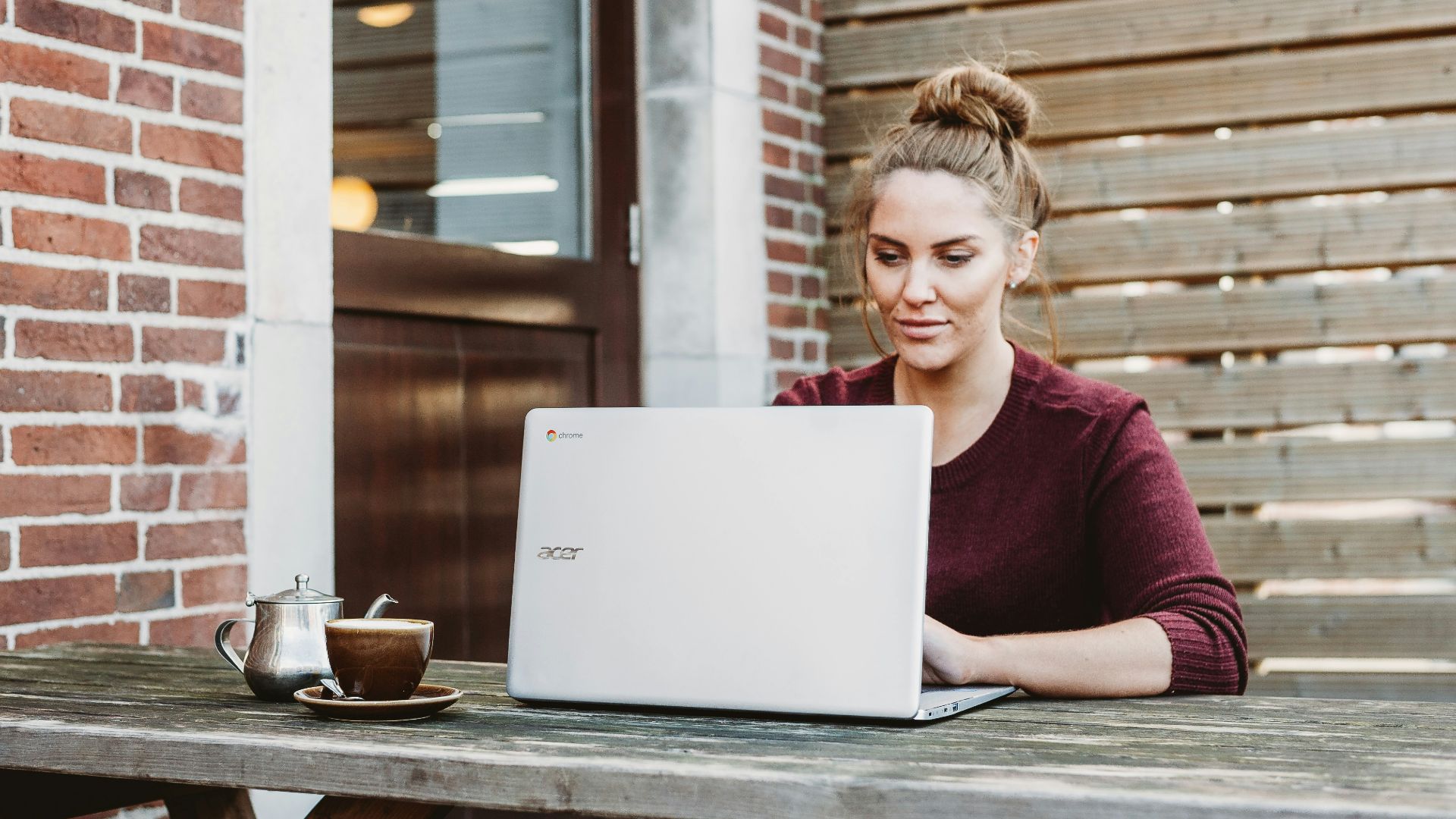 woman sitting and holding white Acer laptop near brown wooden wall