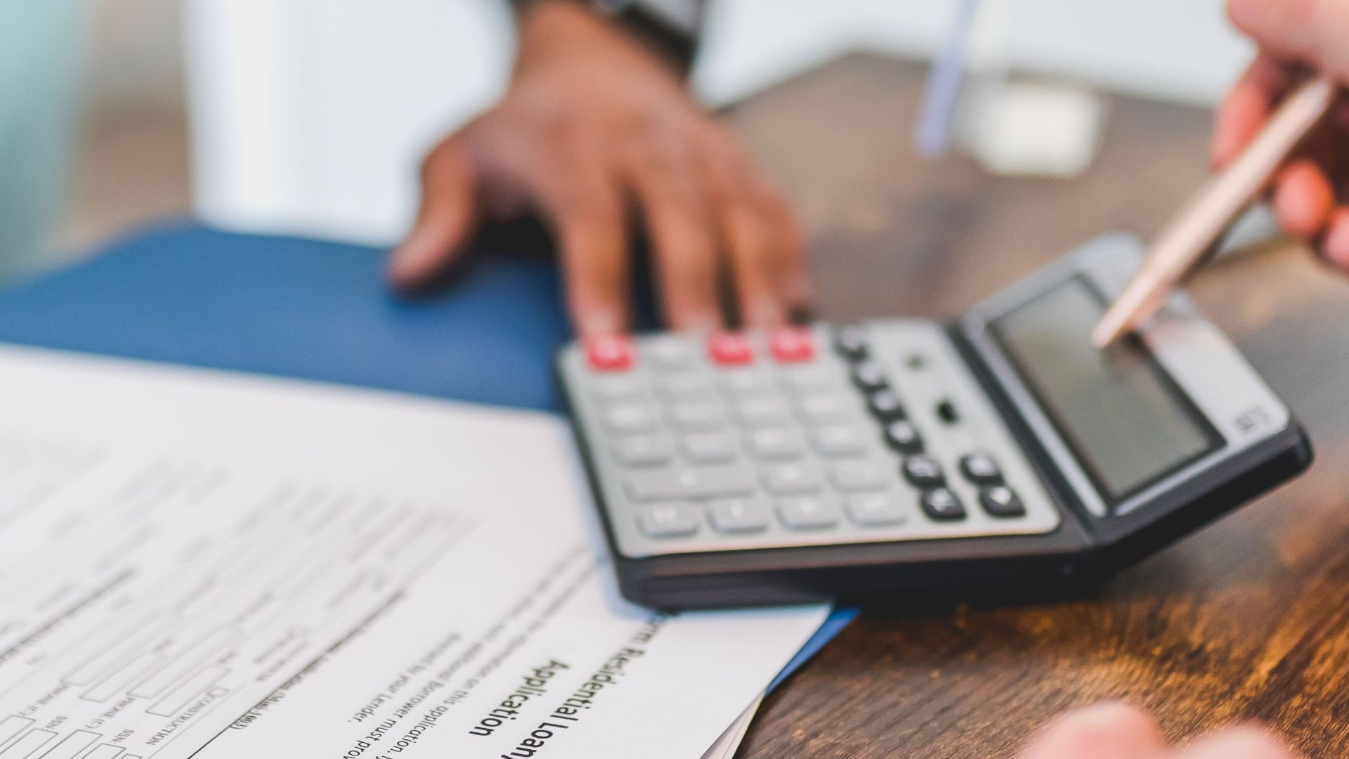 Hands using a calculator with real estate documents on a desk, indicating a financial transaction or meeting.