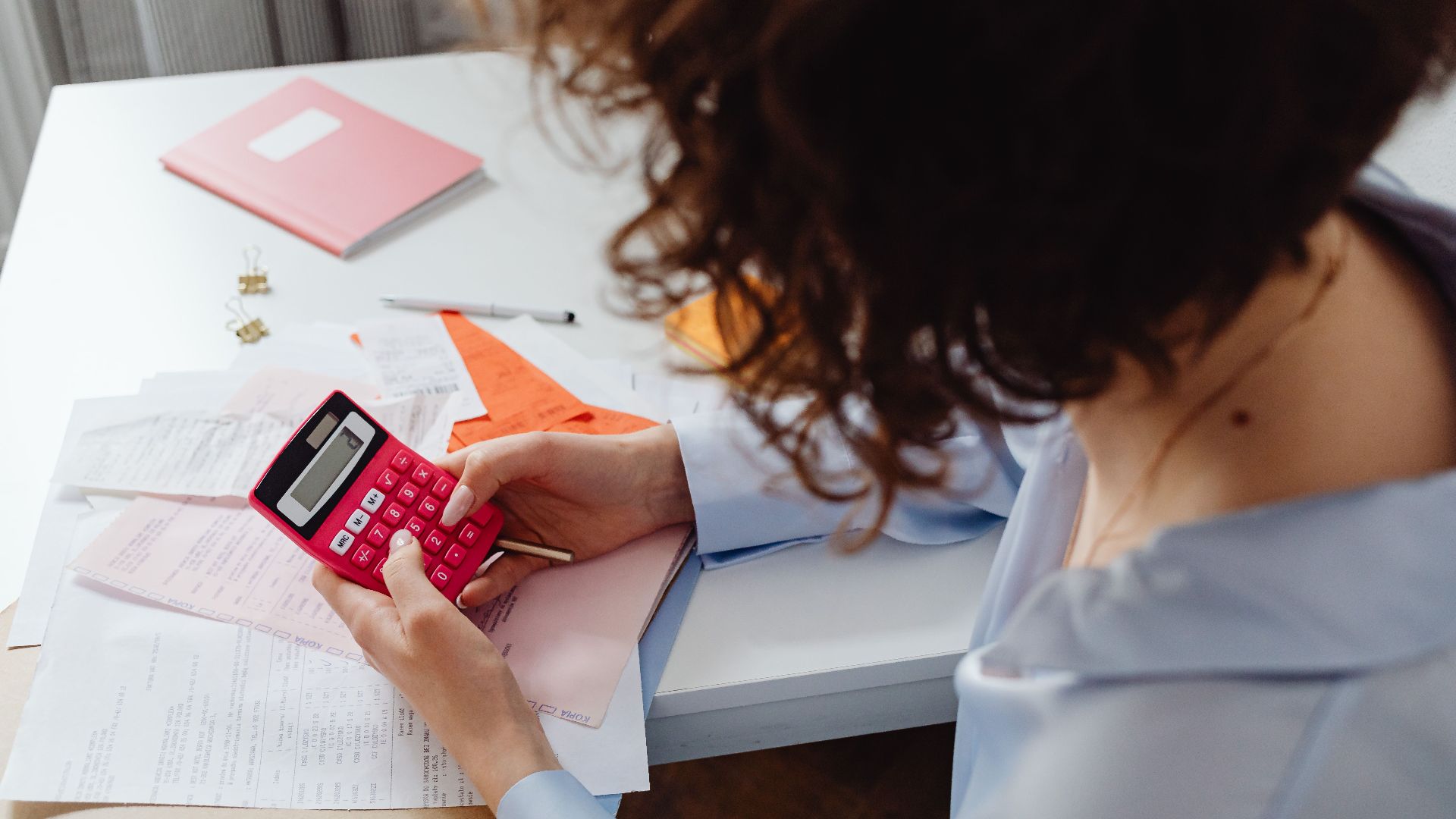 Woman calculating expenses with documents and calculator at work desk.