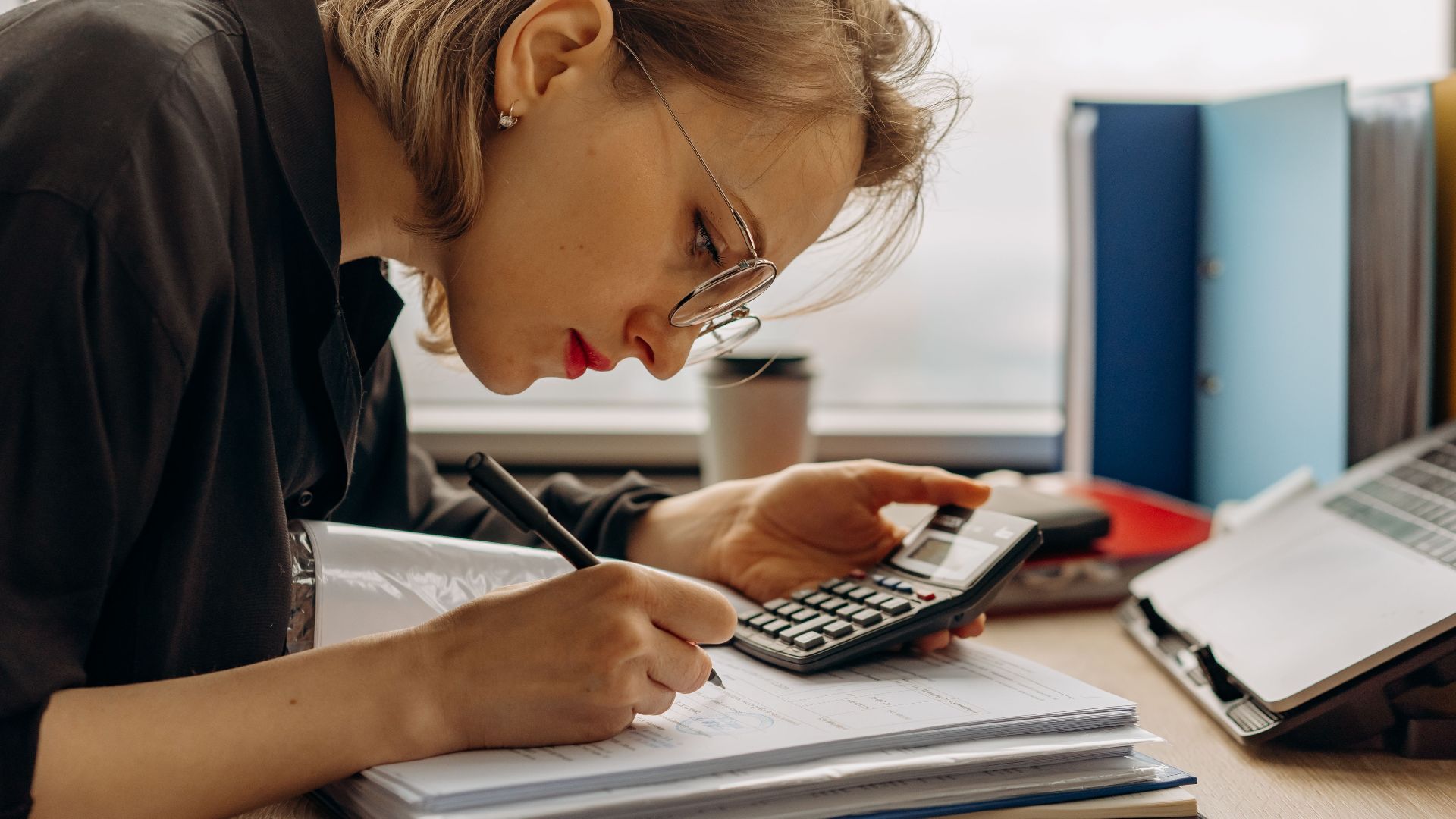 Young woman diligently working on accounting with a calculator and documents. Perfect for business and finance themes.