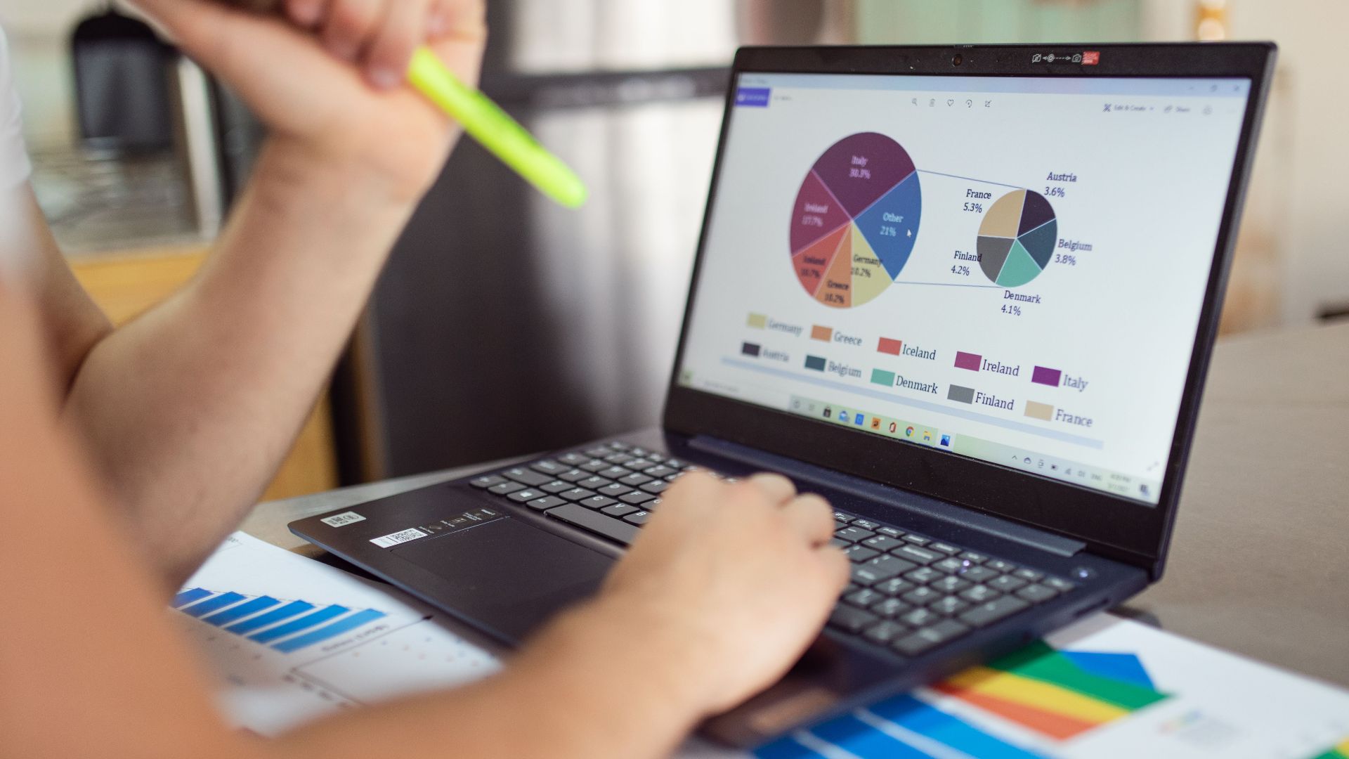 Person analyzing financial charts and graphs on a laptop with colorful documents, showcasing market analysis.