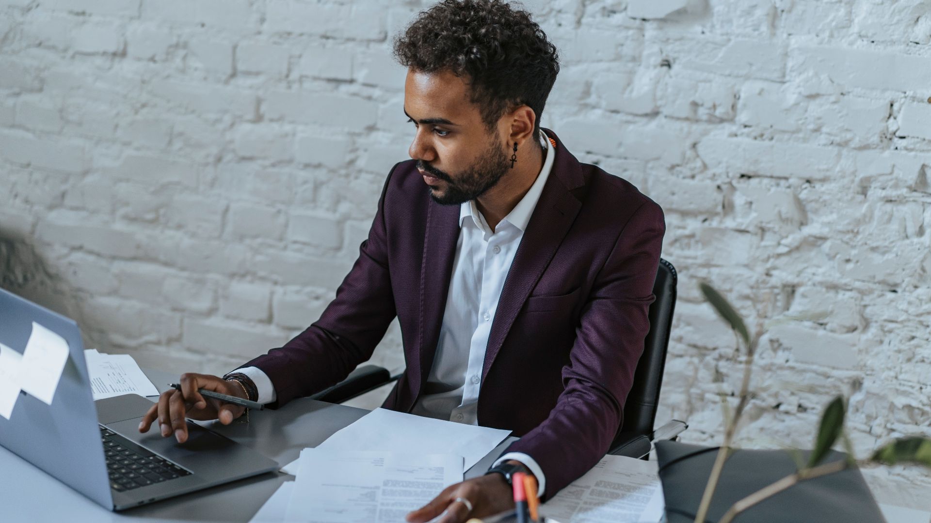 Professional man with curly hair working on a laptop in a stylish office setting.