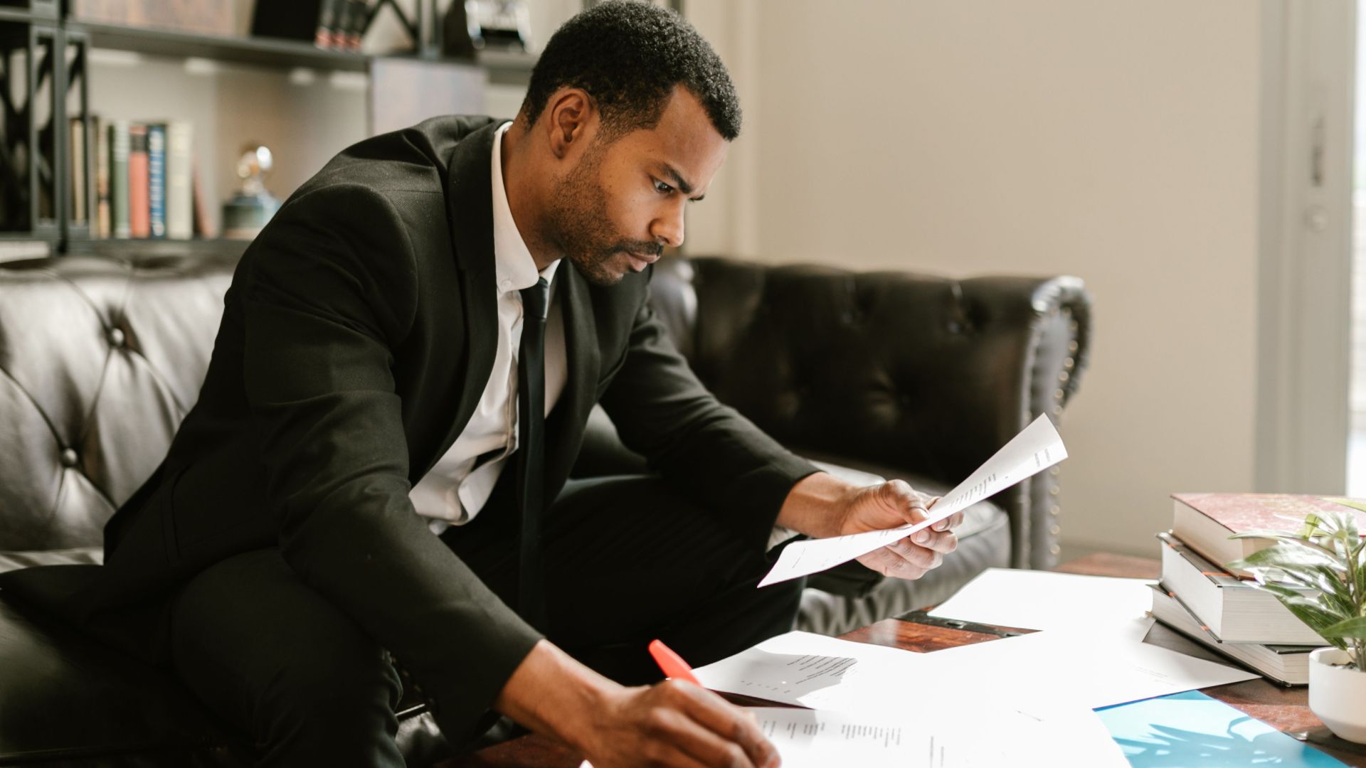 Man in suit signs papers at a coffee table indoors, symbolizing professionalism.
