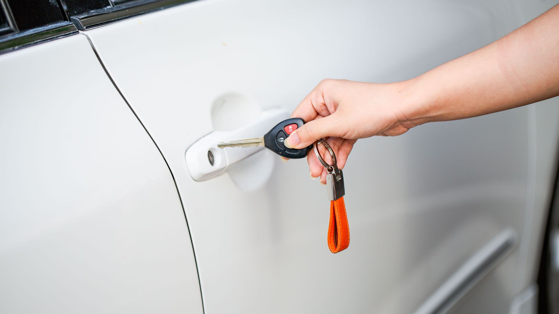 Close-up of a hand unlocking a white car door with a metal key and key fob.
