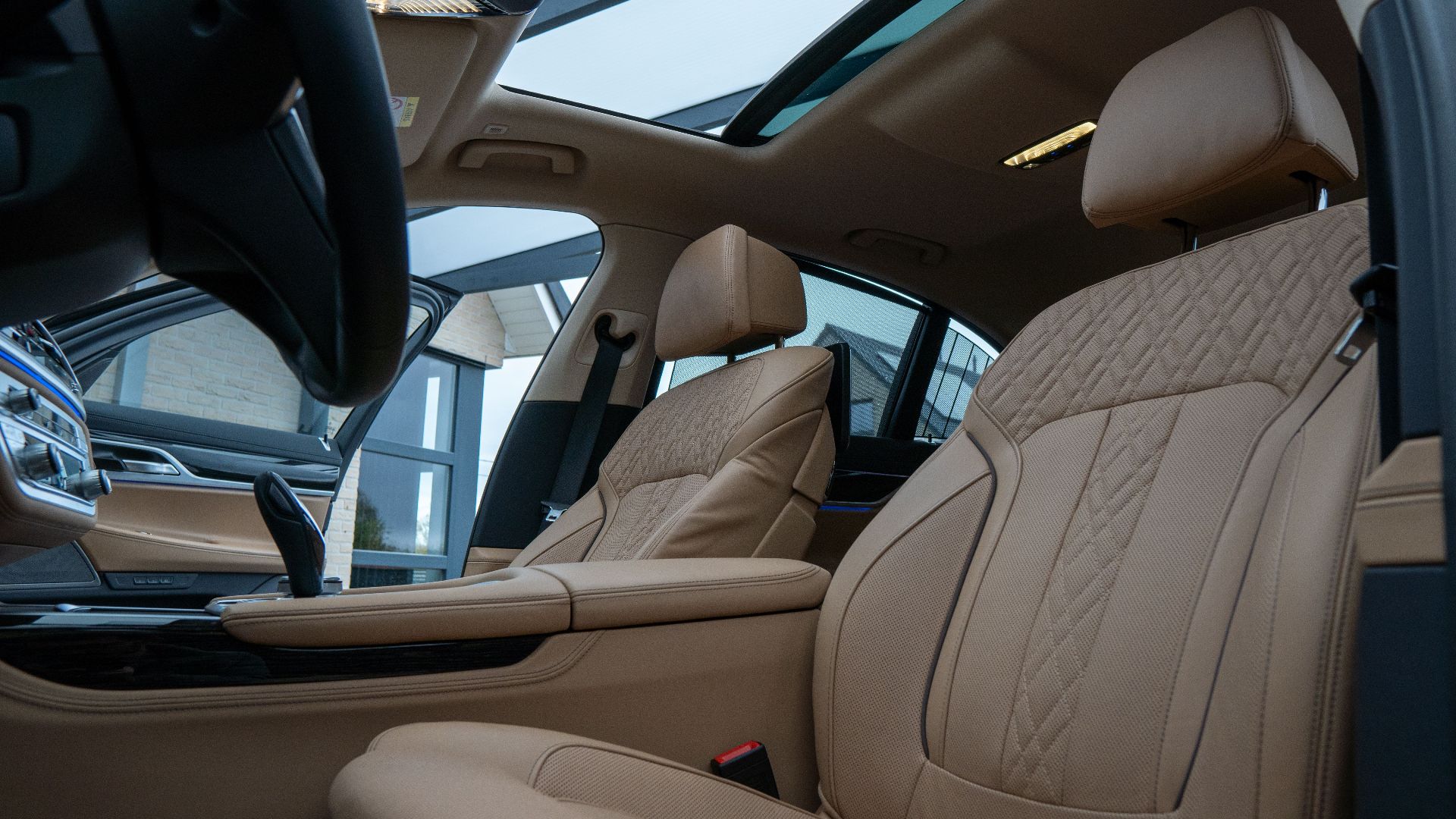 Elegant car interior featuring beige leather seats and a panoramic sunroof, highlighting luxury and comfort.