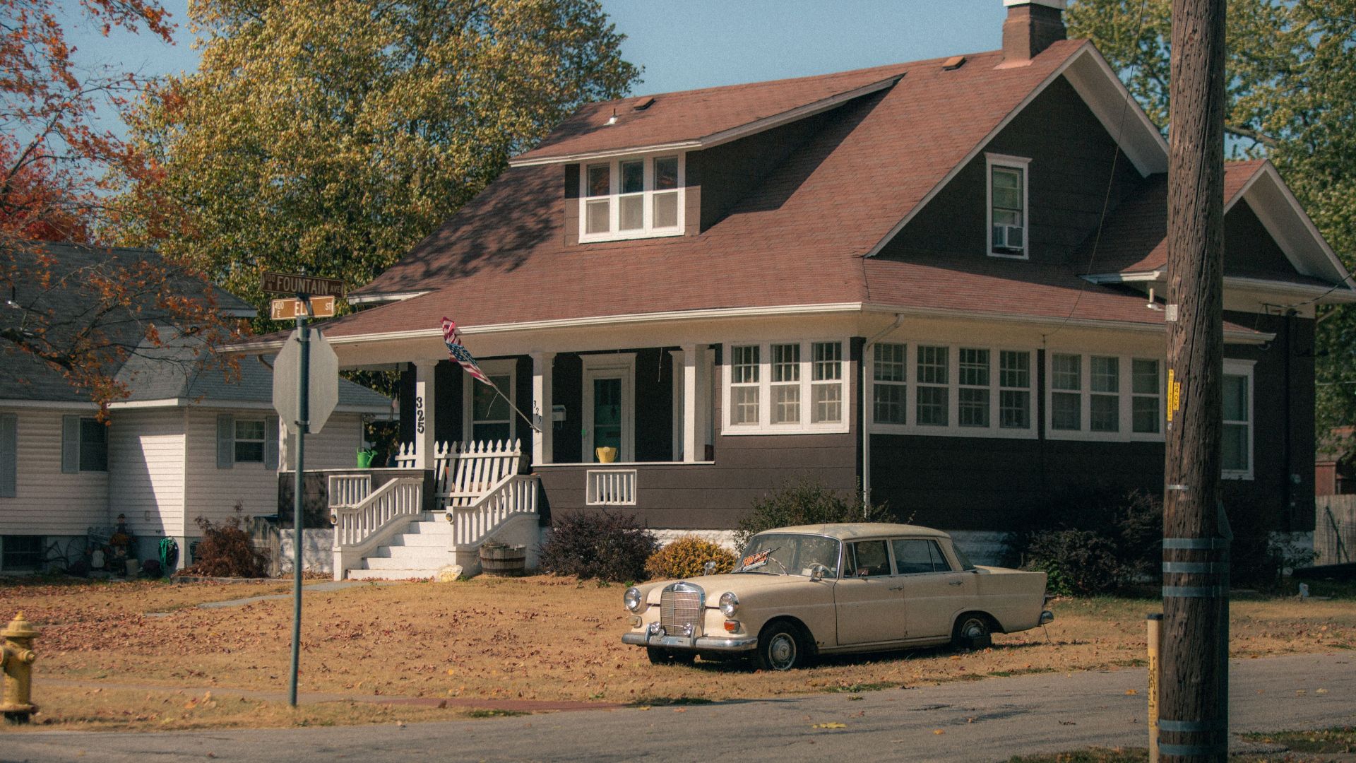 Classic beige car parked by a charming vintage house in a quiet residential area.