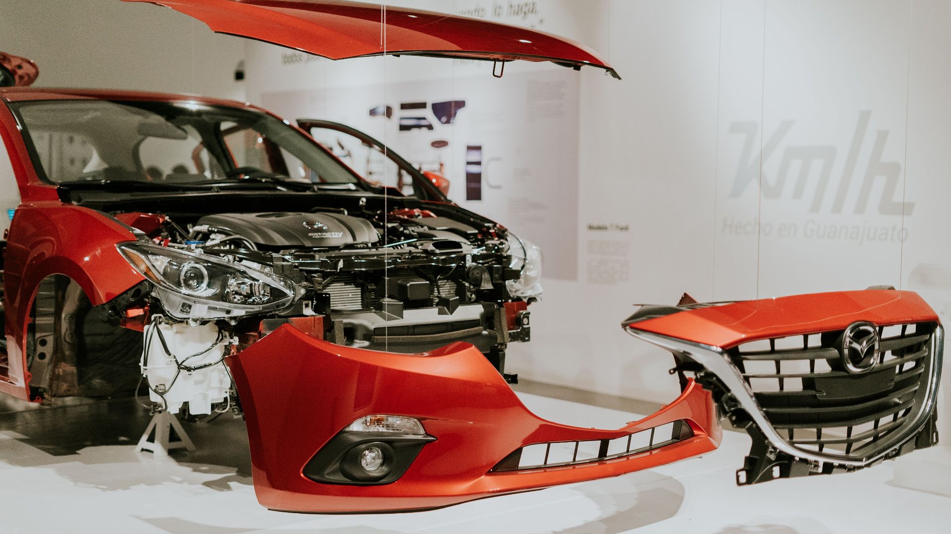 Explore a detailed view of a partially disassembled red Mazda 3 showcased at an auto exhibition.