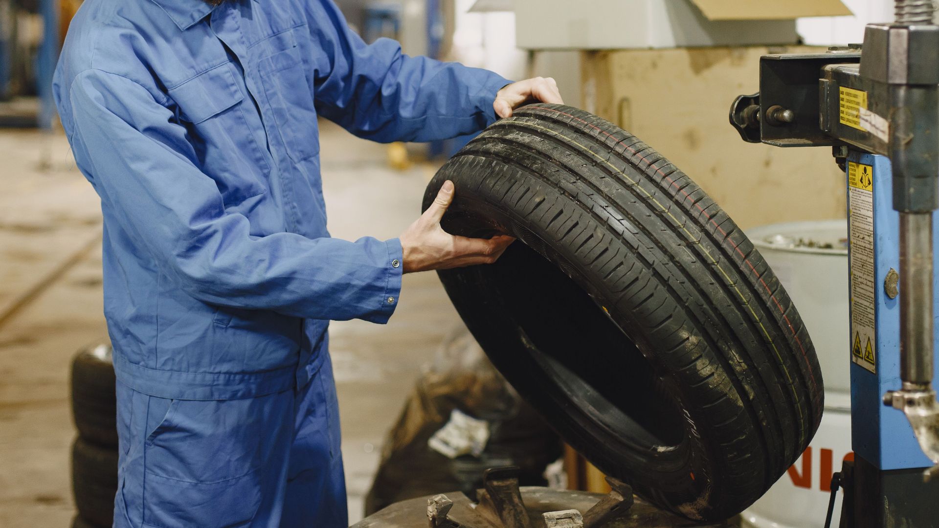 Mechanic in blue uniform examining a tire in an automotive garage.