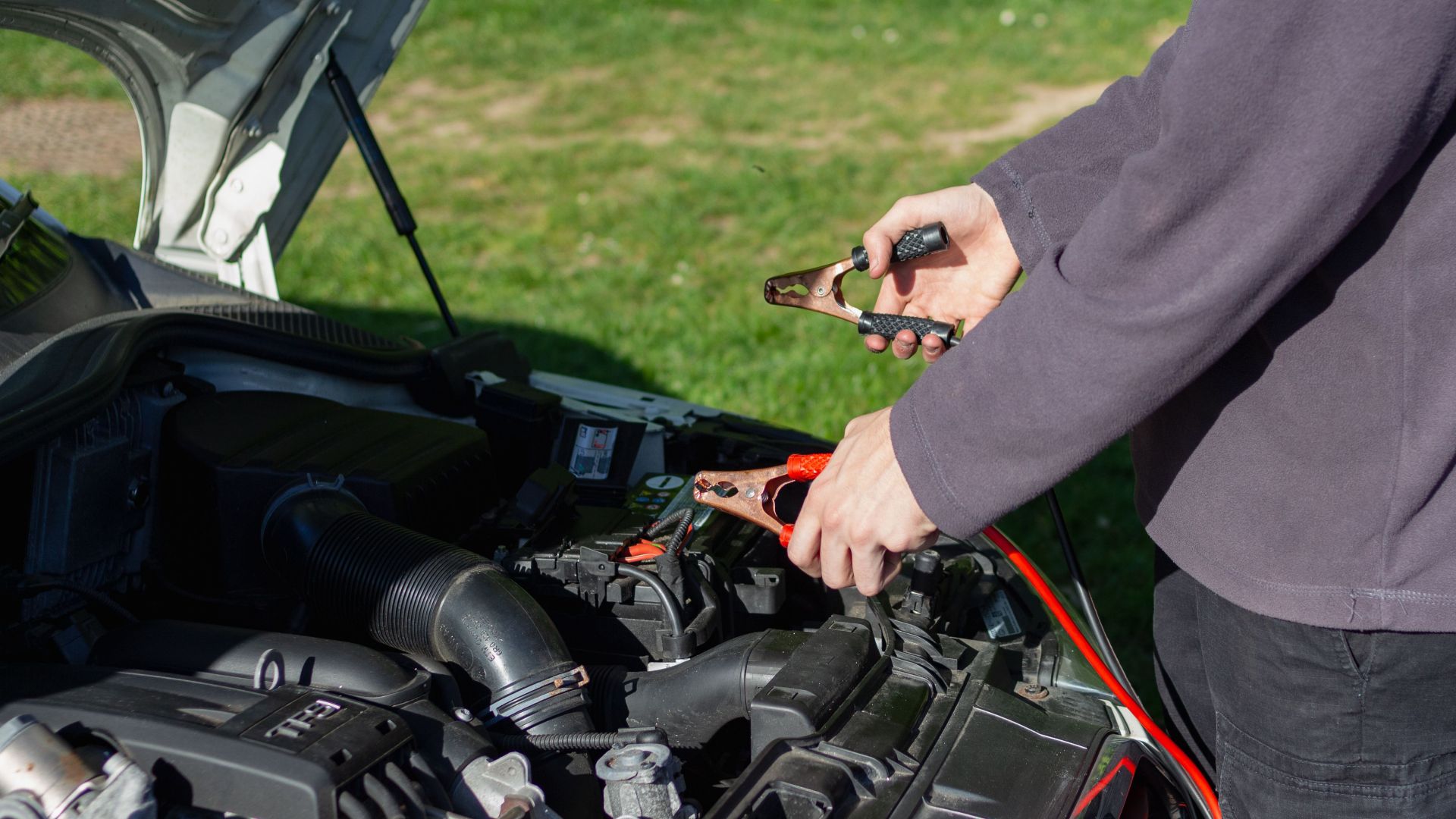 Close-up of mechanic using jumper cables to jump-start a car battery outdoors.