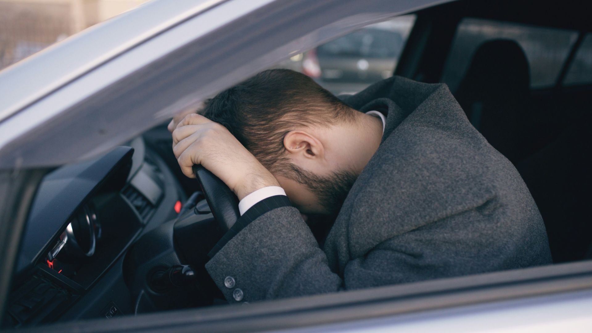 Man resting head on steering wheel inside car