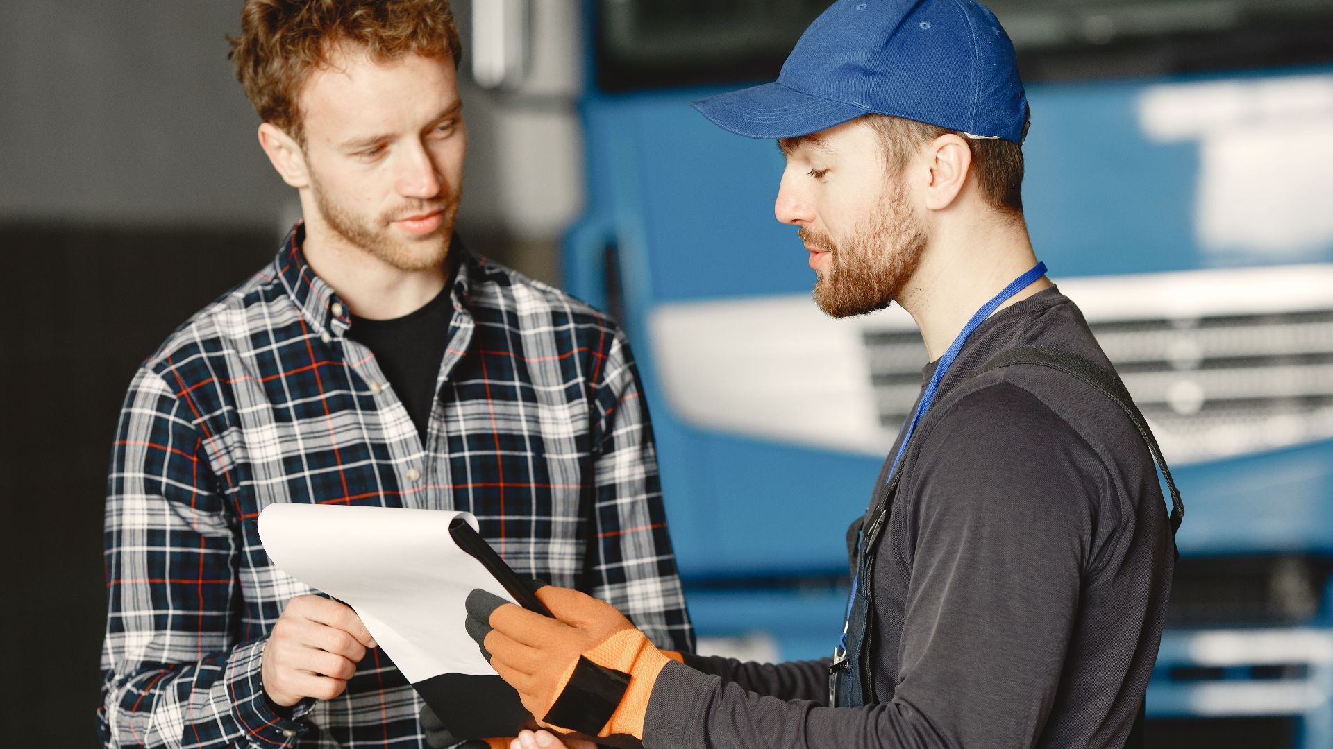 Mechanic in uniform talks with a customer about vehicle maintenance inside a garage.