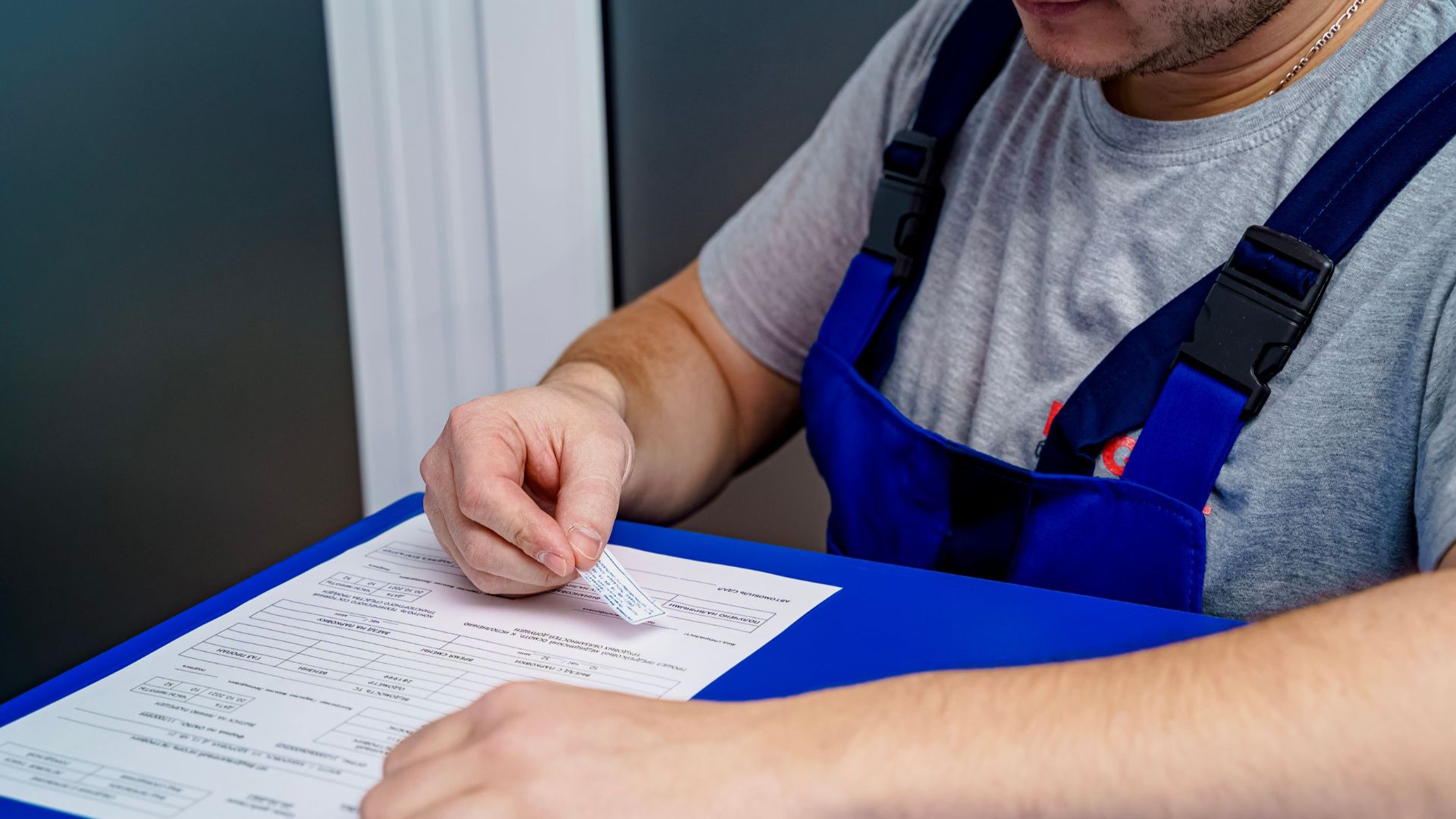 A mechanic in overalls reviews paperwork at a desk in an office setting.
